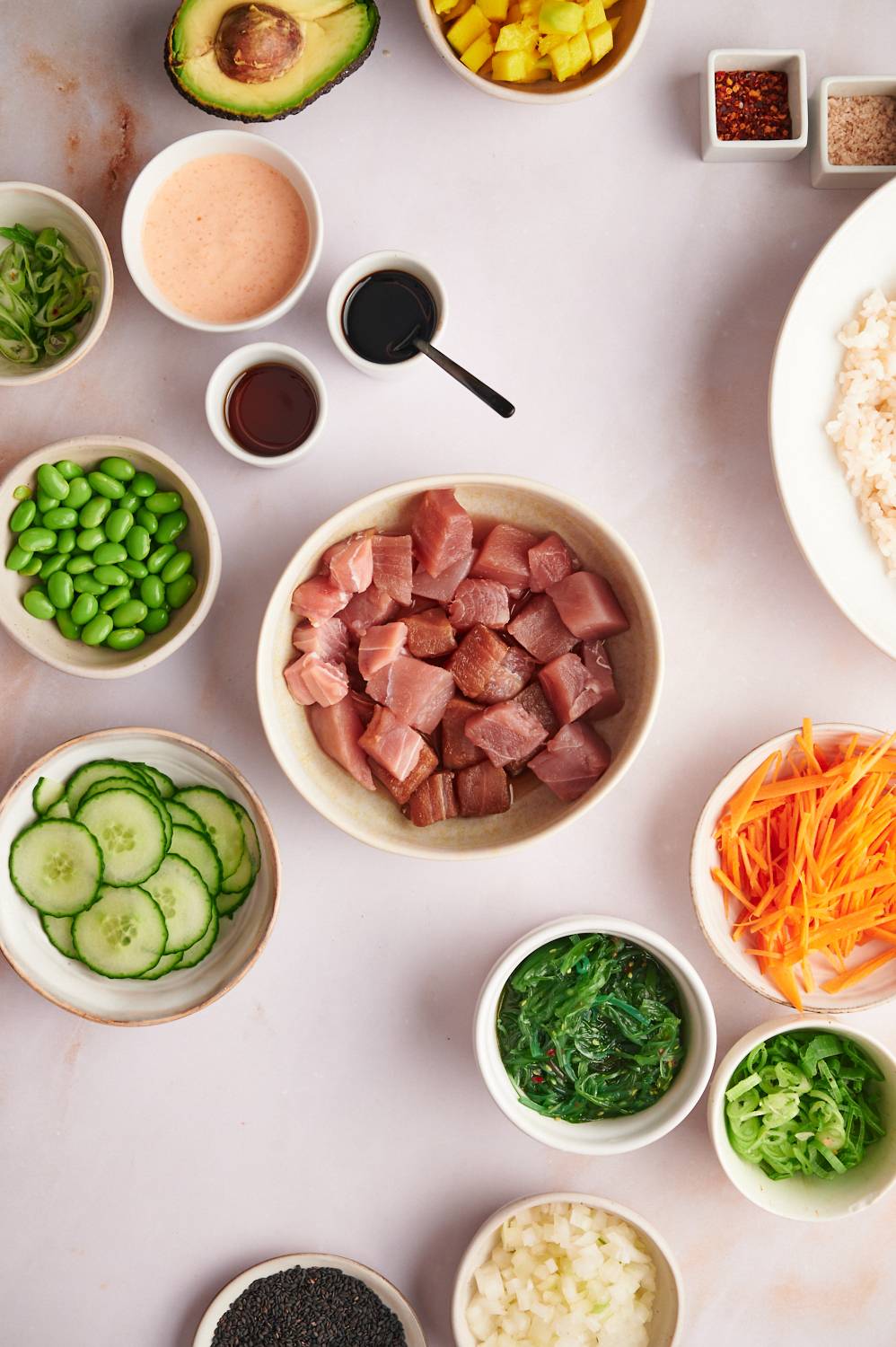 Ingredients for poke bowls with fresh ahi tuna, edamame, cucumbers, scallions, spicy mayo, carrots, and steamed rice.