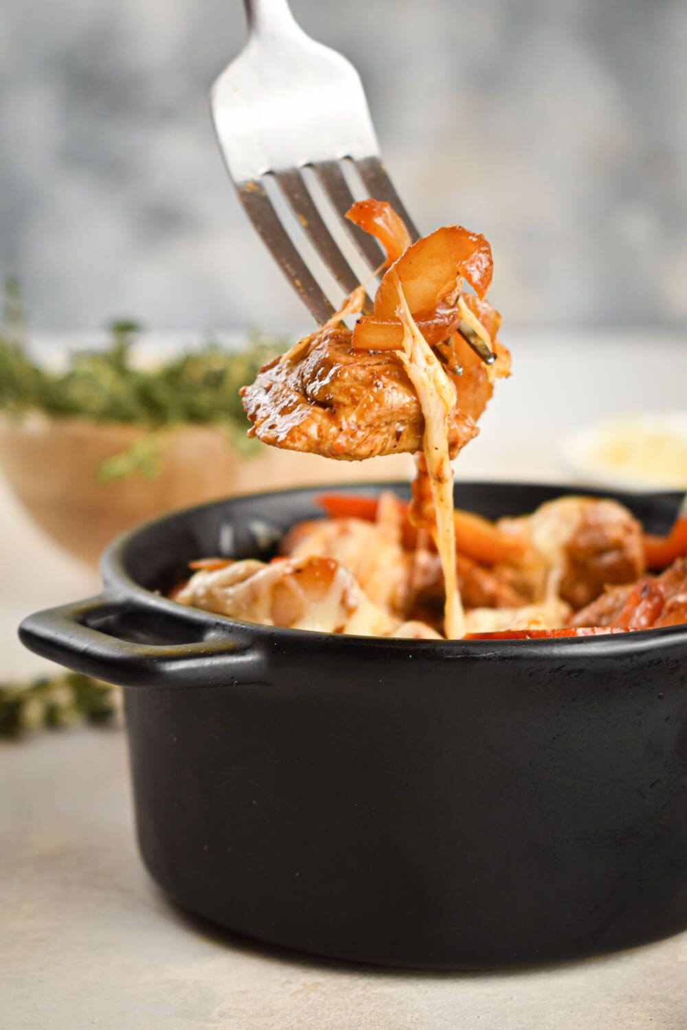 Pork and peppers with melted Parmesan cheese in a cast iron pan with a fork taking a bite.