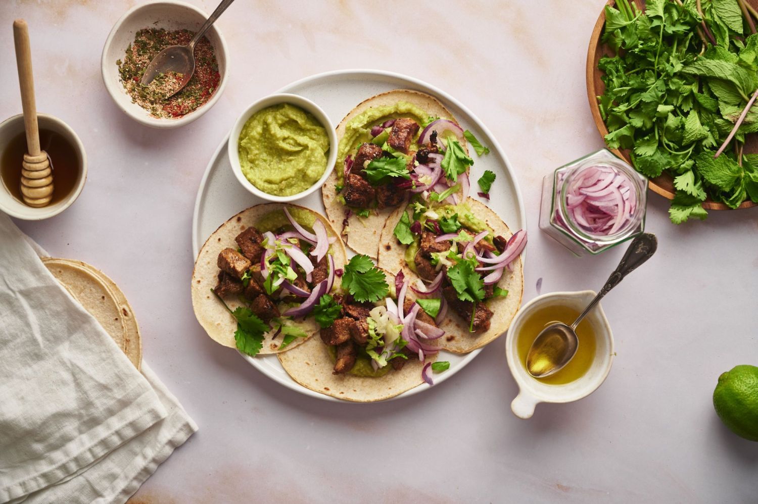 Crispy pork tenderloin tacos served with avocado, pickled onions, cilantro, and corn tortillas on a white plate.