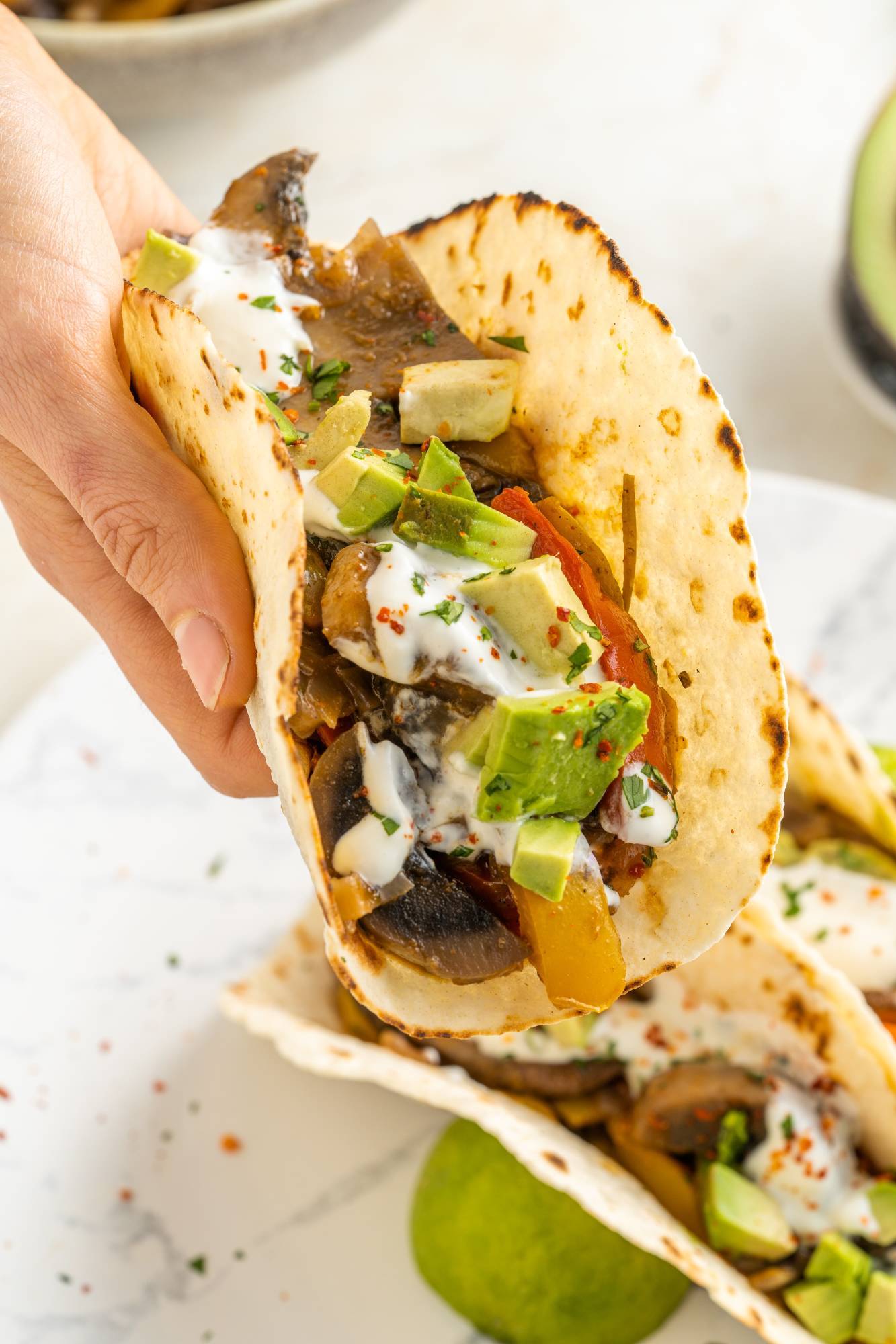 Vegetarian fajitas made with sliced portobello mushrooms, peppers, onions, avocado, and sour cream in a tortilla.