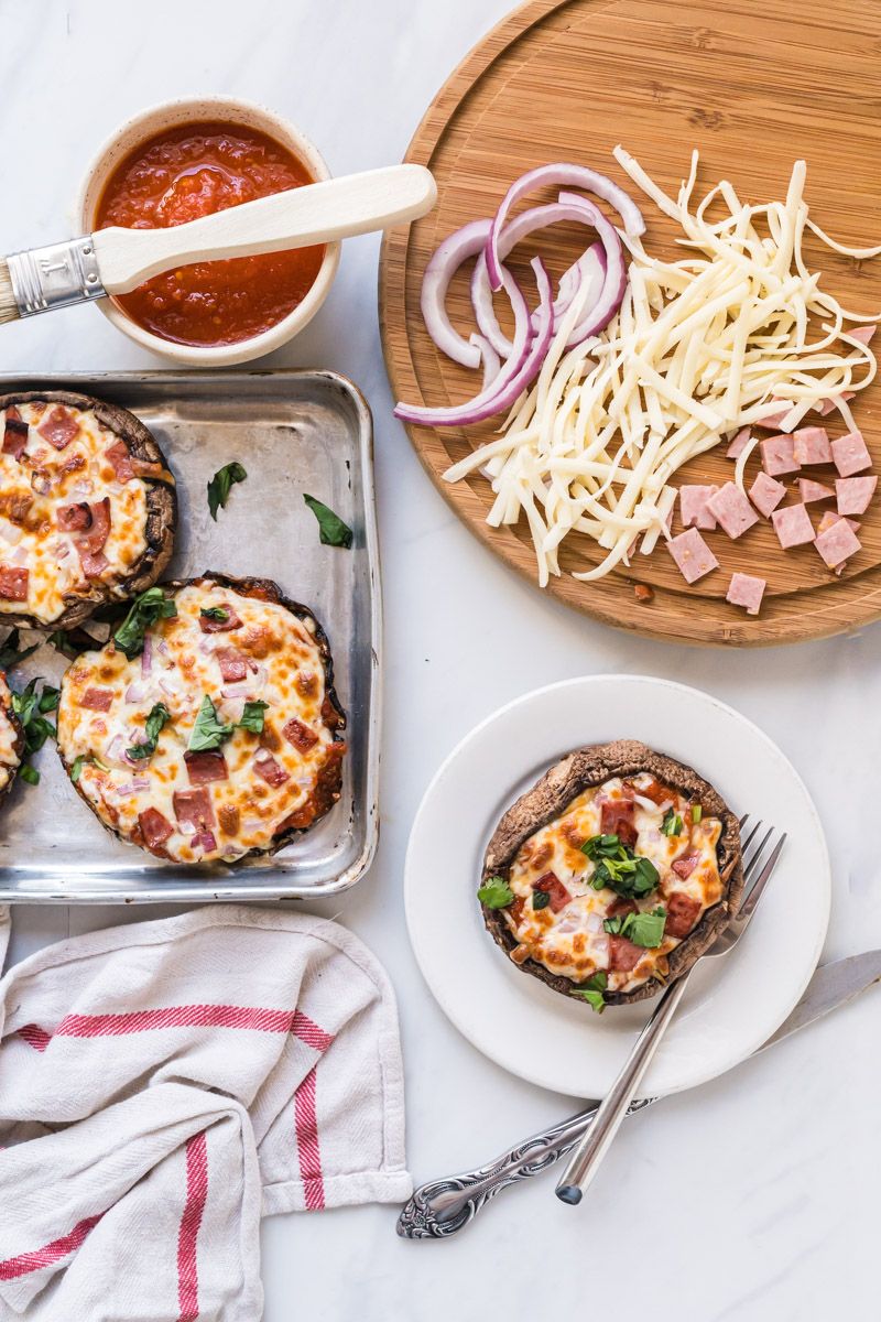 Portobello pizzas with mushroom caps topped with marinara sauce and melted cheese on a plate with a fork.