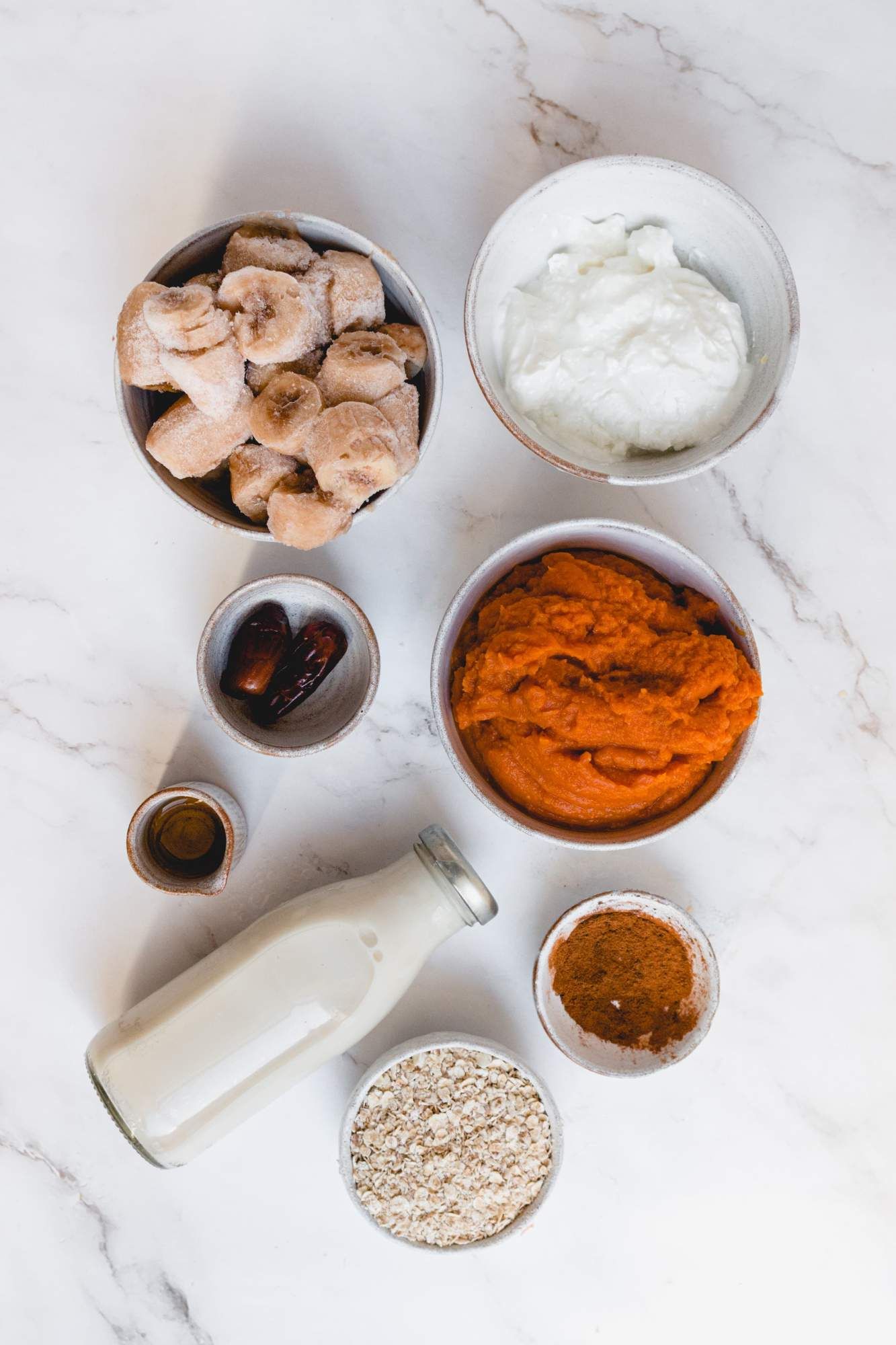 Ingredients for a pumpkin smoothie including pumpkin puree, yogurt, banana, dates, cinnamon, oats, and milk.