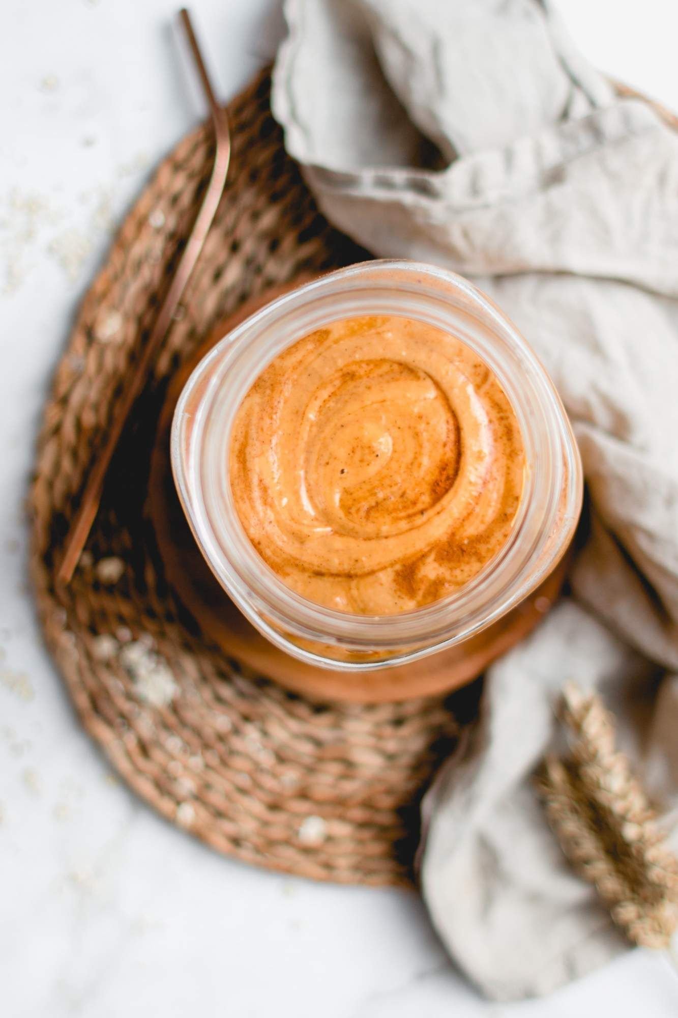 Creamy pumpkin smoothie with oatmeal, pumpkin puree, yogurt, and pumpkin pie spice in a glass with a copper straw.