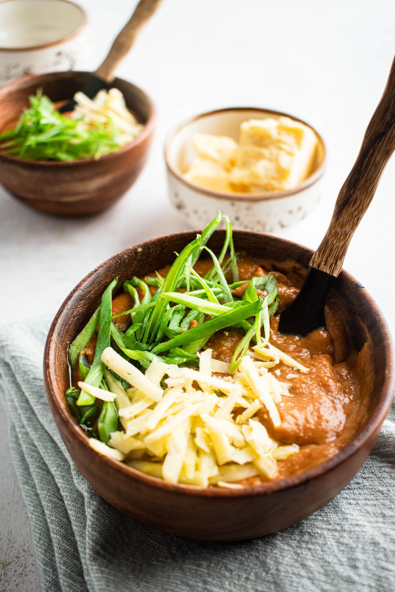 Refried beans made from cooked pinto beans in a bowl with shredded cheese and green onions.