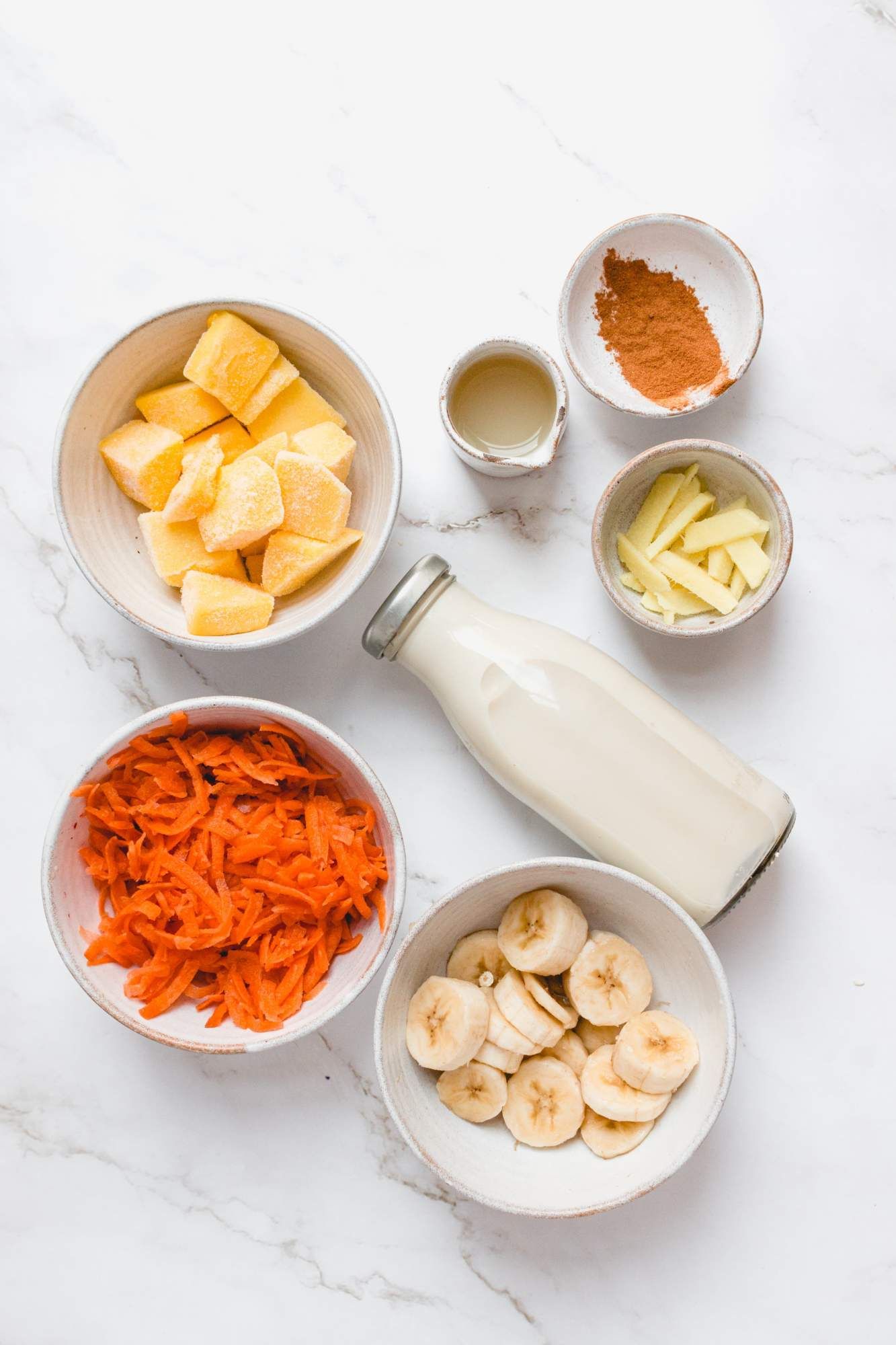 Ingredients for a carrot smoothie with shredded carrots, ginger, banana, mango, and almond milk.