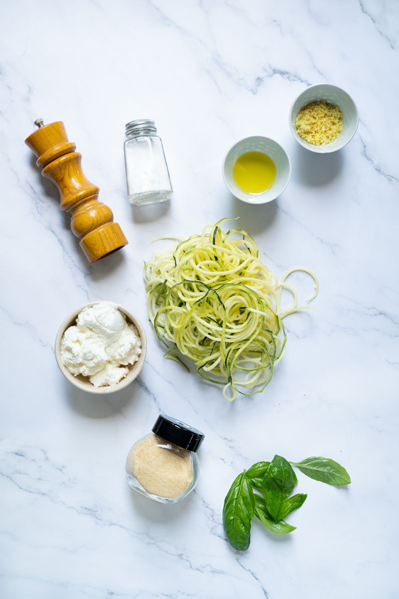 Ingredients for ricotta zucchini noodles including fresh zoodles, basil, garlic powder, ricotta cheese, and lemon zest.