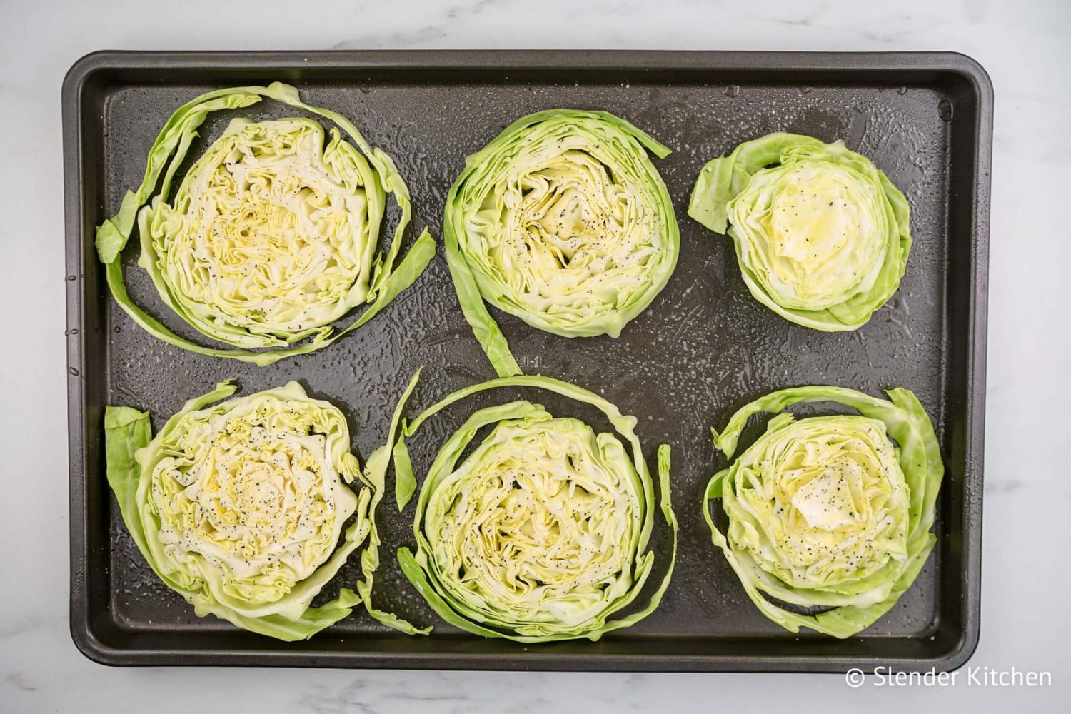 Cabbage slices on a sheet pan with olive oil, salt, and pepper.