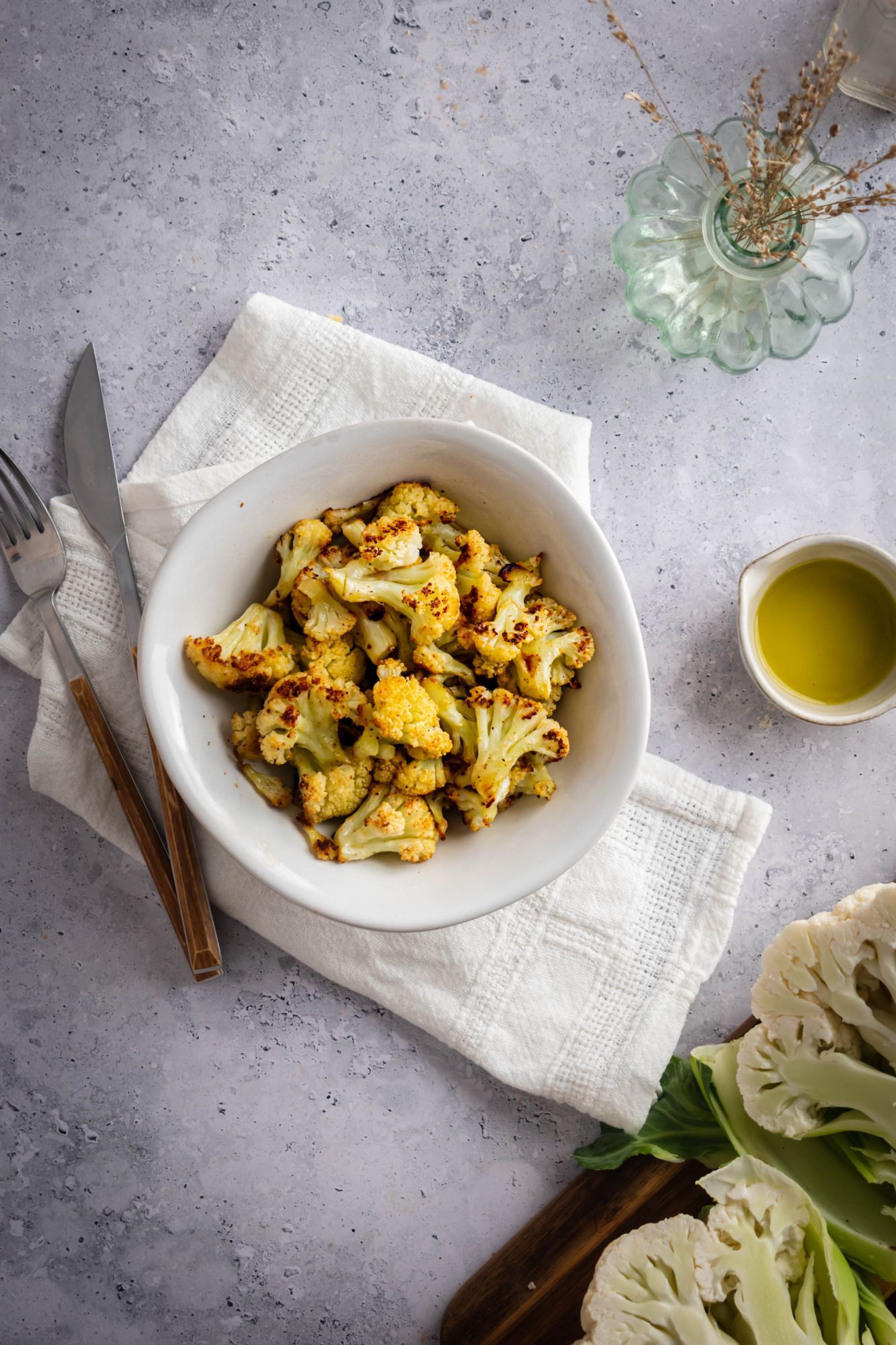 Cauliflower that has been roasted with browned edges in a bowl with olive oil on the side.