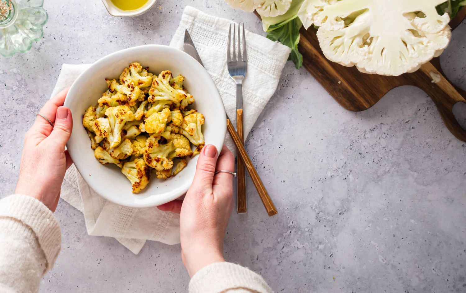 Crispy roasted cauliflower florets in a bowl with a whole cauliflower on the side.