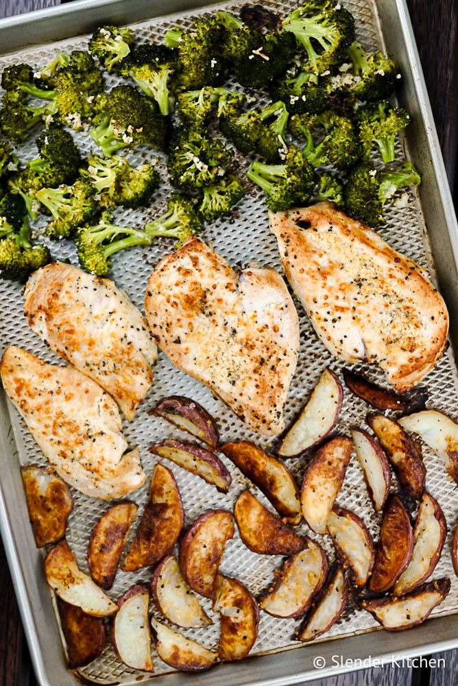 Chicken and potatoes with broccoli on a silver baking sheet with minced garlic.