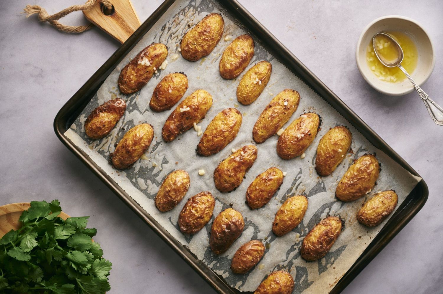 Baking sheet with roasted fingerling potatoes drizzled with butter and garlic.