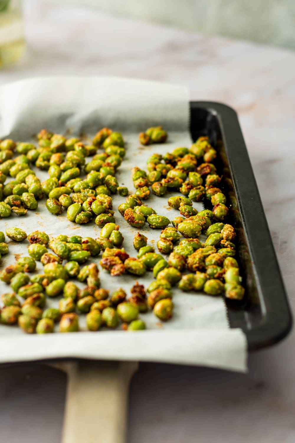 Roasted edamame with crispy Parmesan cheese and garlic on a baking sheet.