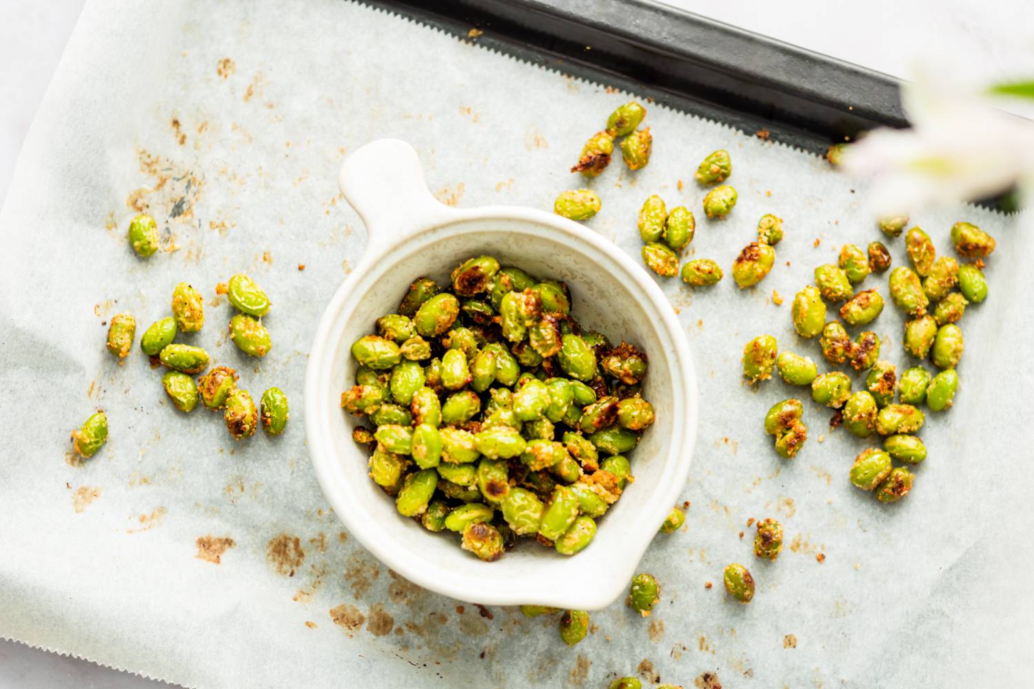 Roasted shelled edamame with garlic served in a small bowl on a baking sheet.