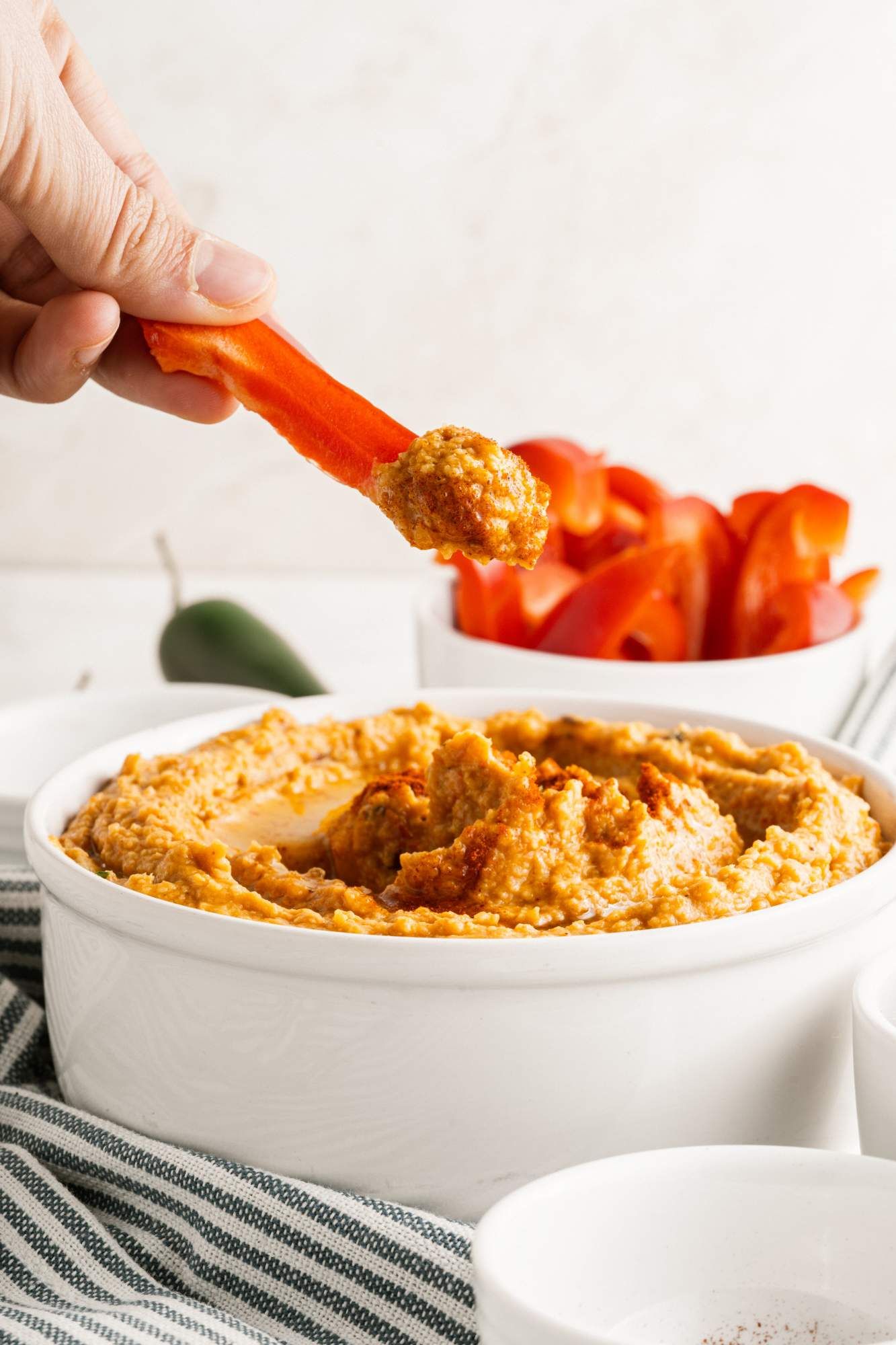 Red pepper white bean dip with a hand dipping in a slice of bell pepper.