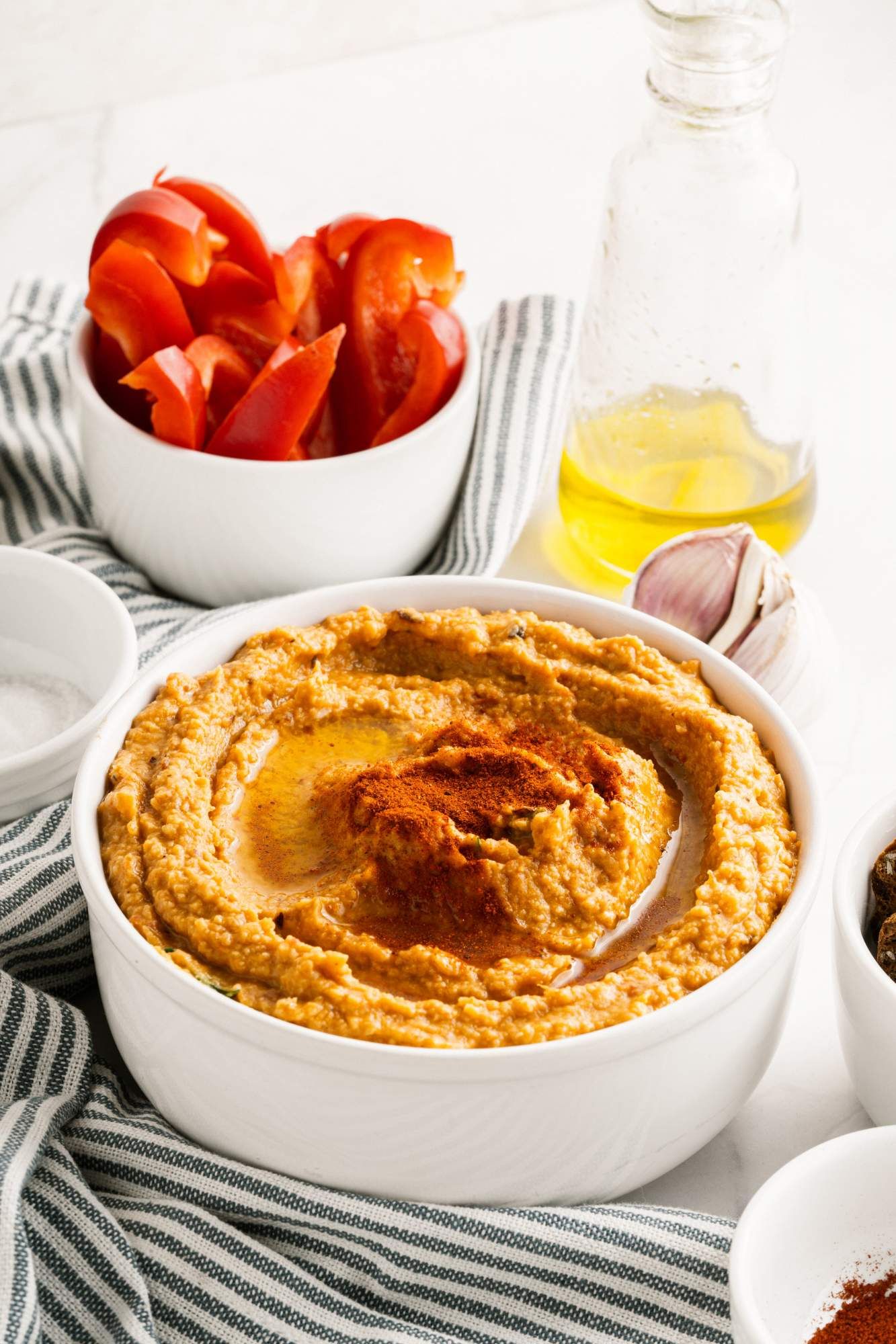 Roasted red pepper and white bean dip in a bowl with olive oil, garlic, and sliced red bell peppers.