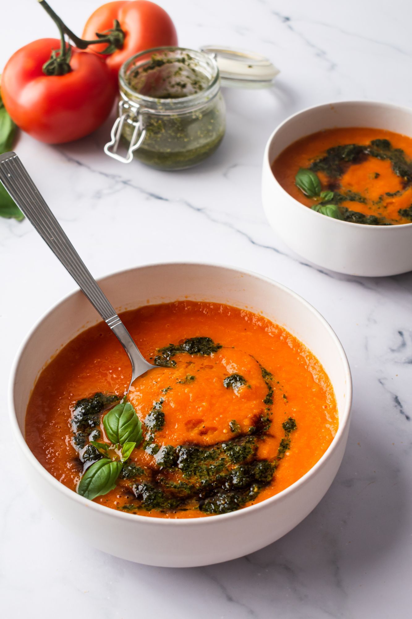 Bowl of tomato basil soup with drizzled pesto and fresh basil leaves.