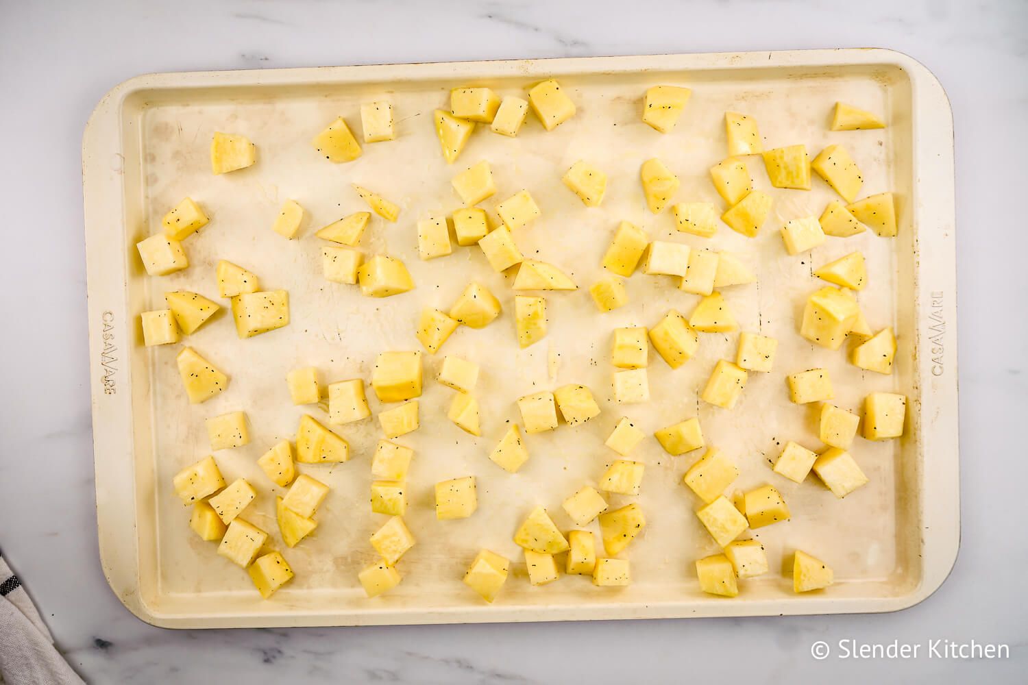 Chopped turnips with salt, pepper, and olive oil on a roasting pan.