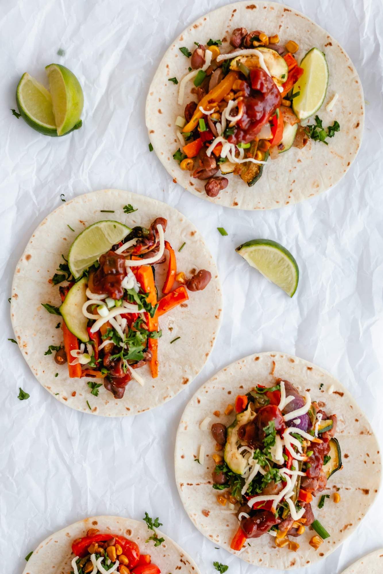 Roasted vegetable fajitas with peppers, zucchini, corn, carrots, and pinto beans in tortillas with shredded cheese.