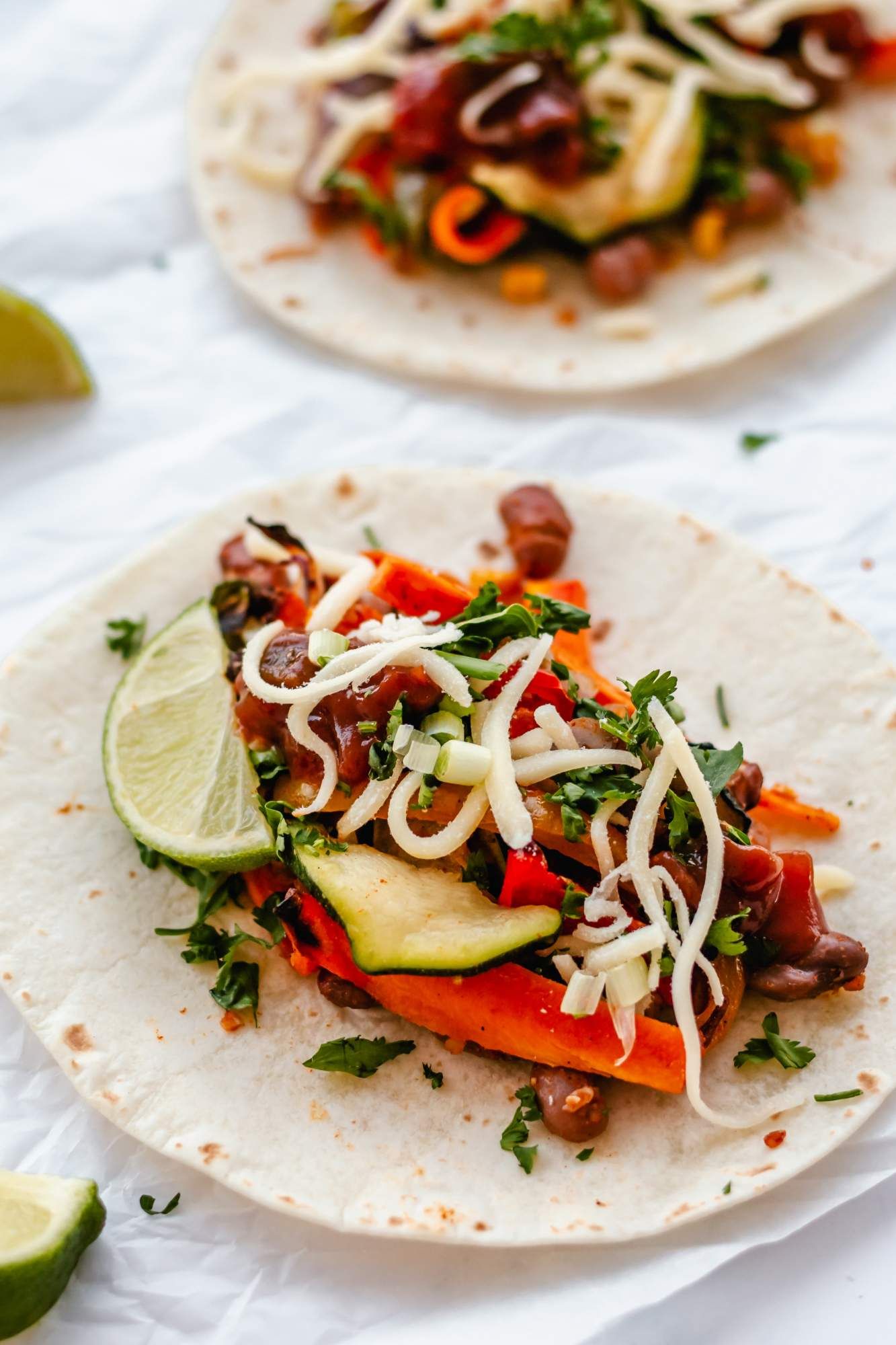 Vegetables fajitas with roasted vegetables, corn, and pinto beans in a tortilla with shredded cheese and limes.