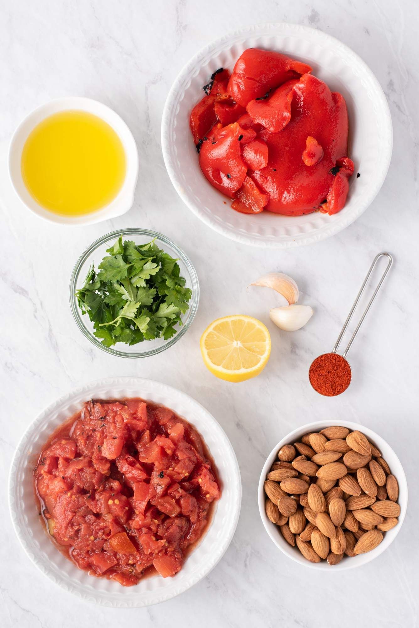 Ingredients for romesco sauce including roasted tomatoes, red peppers, olive oil, almonds, garlic, parsley, and lemon.