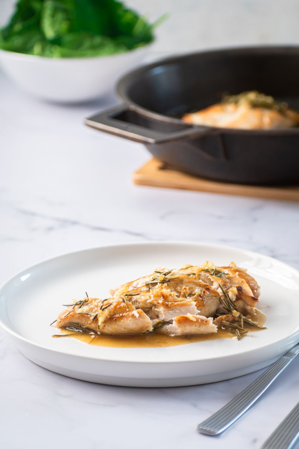 Skillet rosemary chicken with garlic, lemon, and butter sliced on a plate with a skillet in the background.