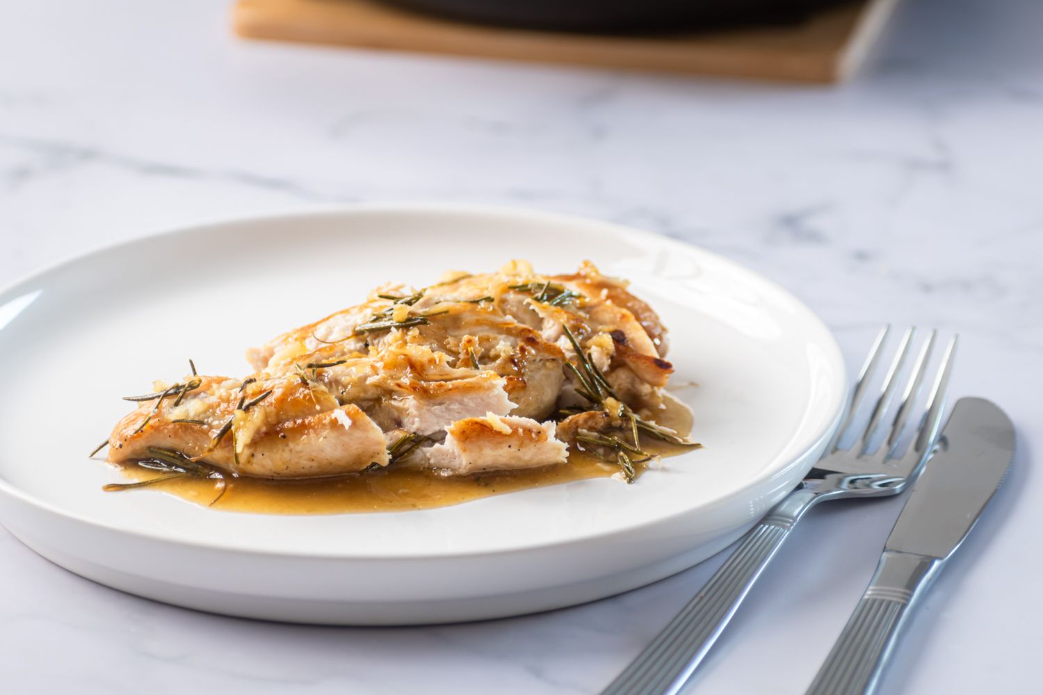 Sliced rosemary chicken breast on a plate with fresh rosemary and a lemon and garlic pan sauce.