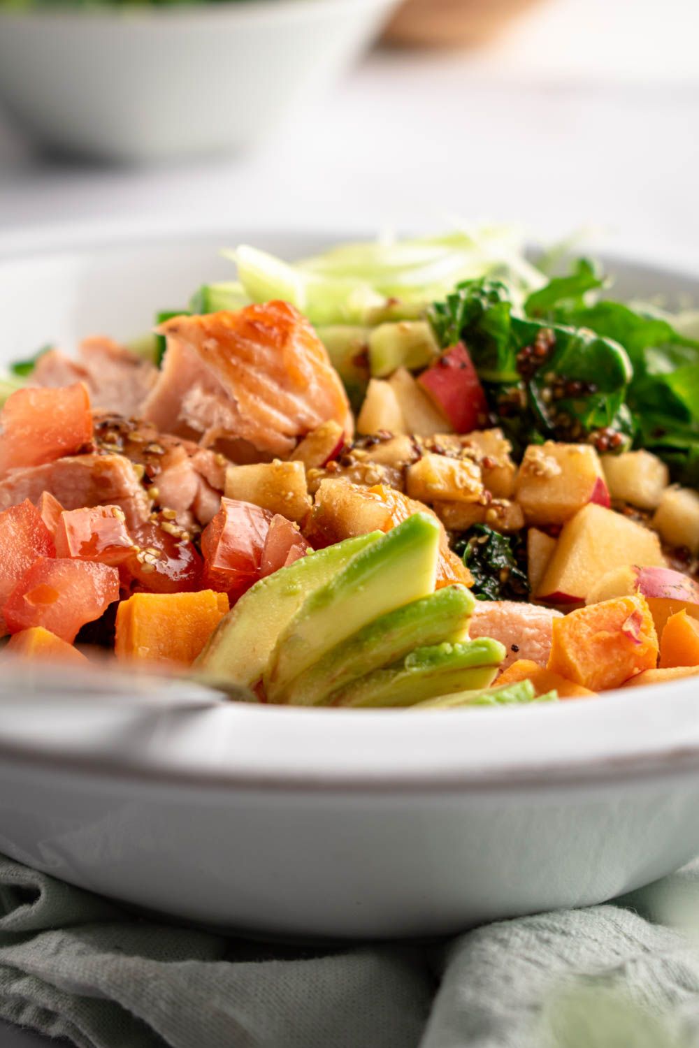 Kale salad with roasted salmon, sweet potatoes, avocado, and apples in a bowl with mustard dressing.