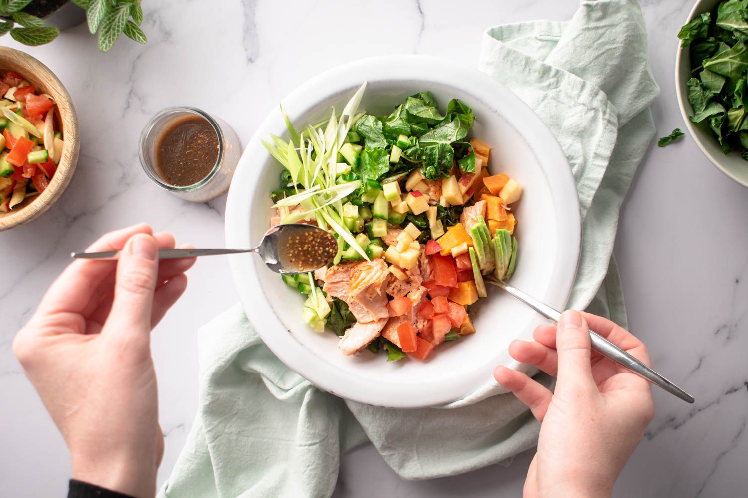 Salmon, sweet potato, and kale salad with apples, green onions, and a maple dijon dressing being spooned on top.