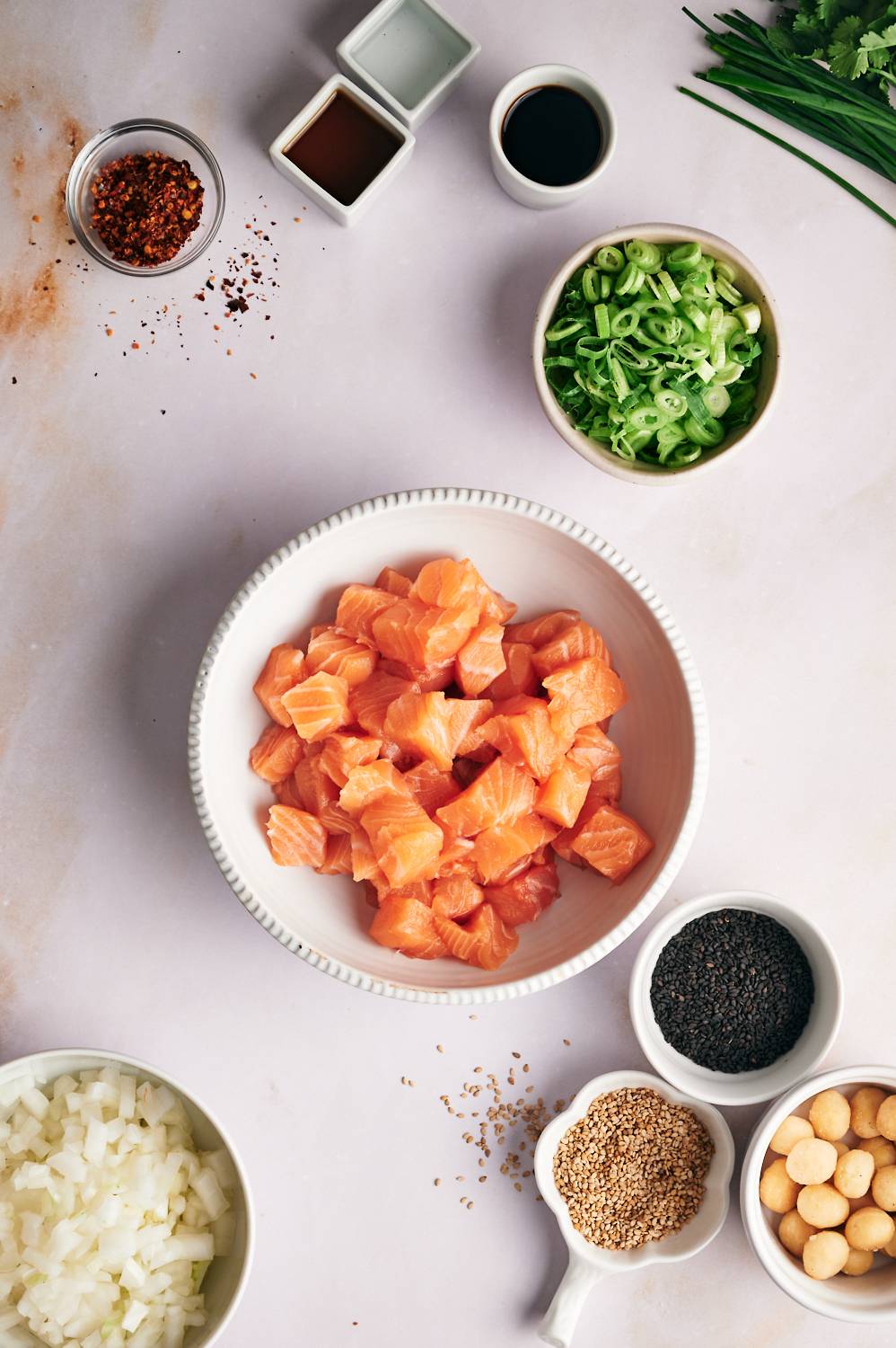 Ingredients to make salmon poke including cubed raw salmon, green onions, sesame seeds, soy sauce, sesame oil, and chopped onions.