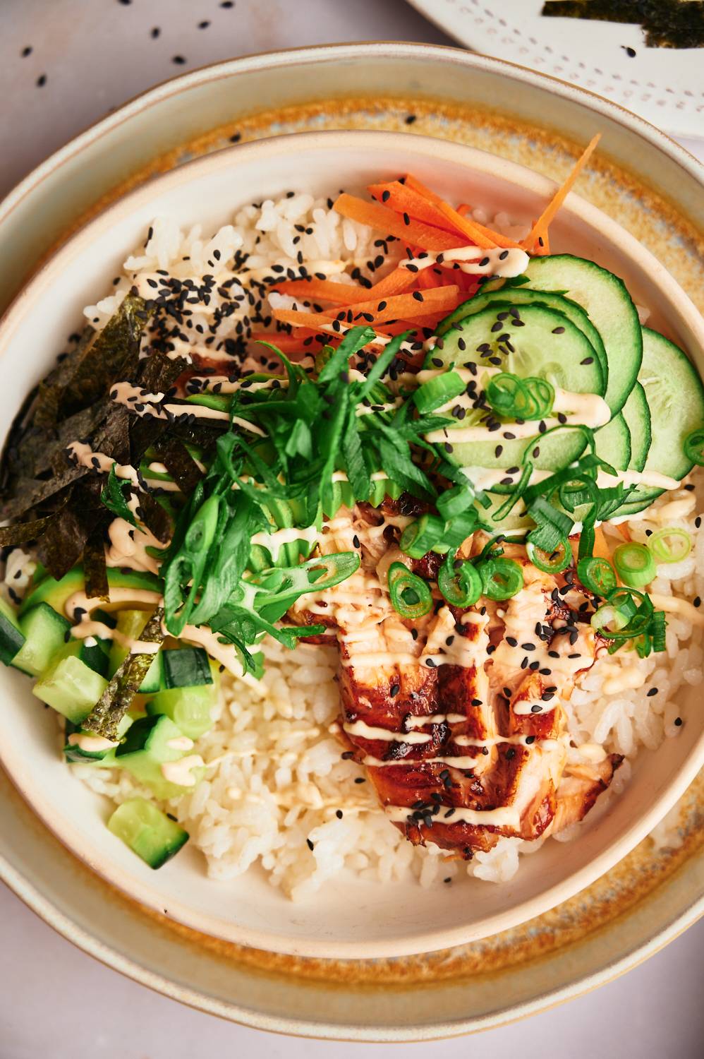 Easy salmon sushi bowls with nori, cucumbers, carrots, sushi rice, sesame seeds, and spicy mayo.