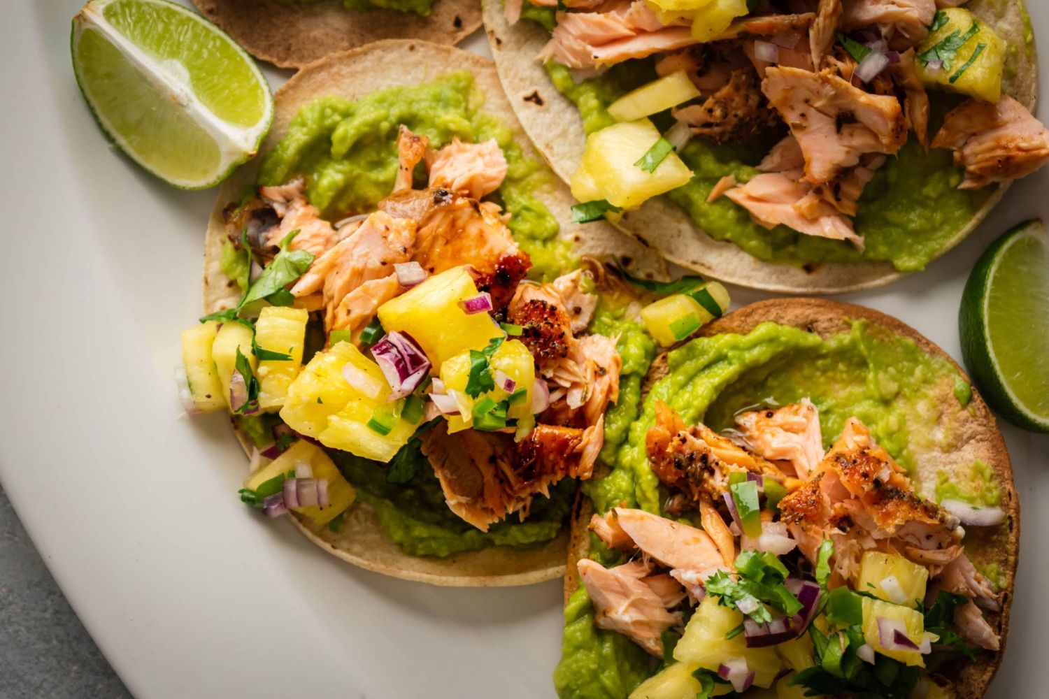 Tostadas with baked salmon, pineapple salsa, cilantro, red onion, and creamy avocado on yellow corn tortillas.