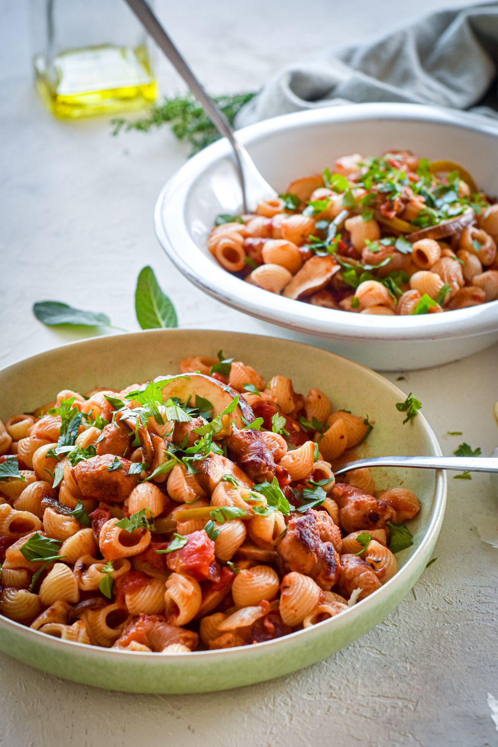 Pasta with sausage and peppers in two bowls with sliced peppers, mushrooms, turkey sausage, and garlic.