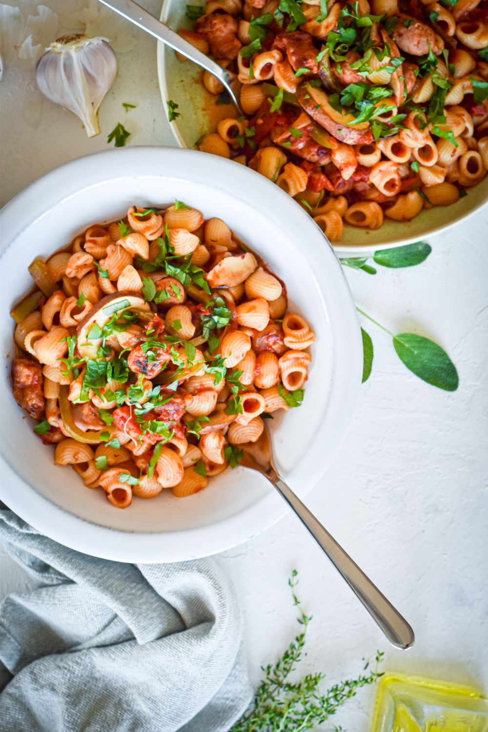 Sausage pasta with bell peppers, onions, and mushrooms with a garlic tomato sauce in a white bowl.