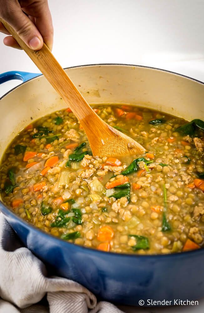 Lentil sausage soup with lentils, sausage, carrots, celery, onions, and garlic in a large pot with a hand stirring.