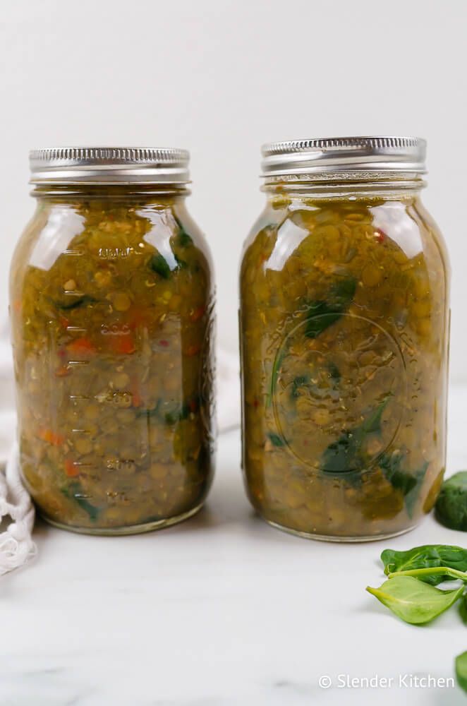 Sausage and lentil soup in two glass mason jars with some fresh spinach.