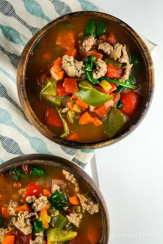 Sausage and pepper soup with spinach, carrots, celery, and ground sausage in two wooden bowls.