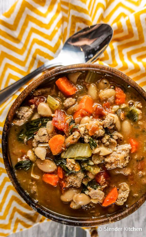 White bean sausage and spinach soup on a bowl with a spoon and yellow napkin.