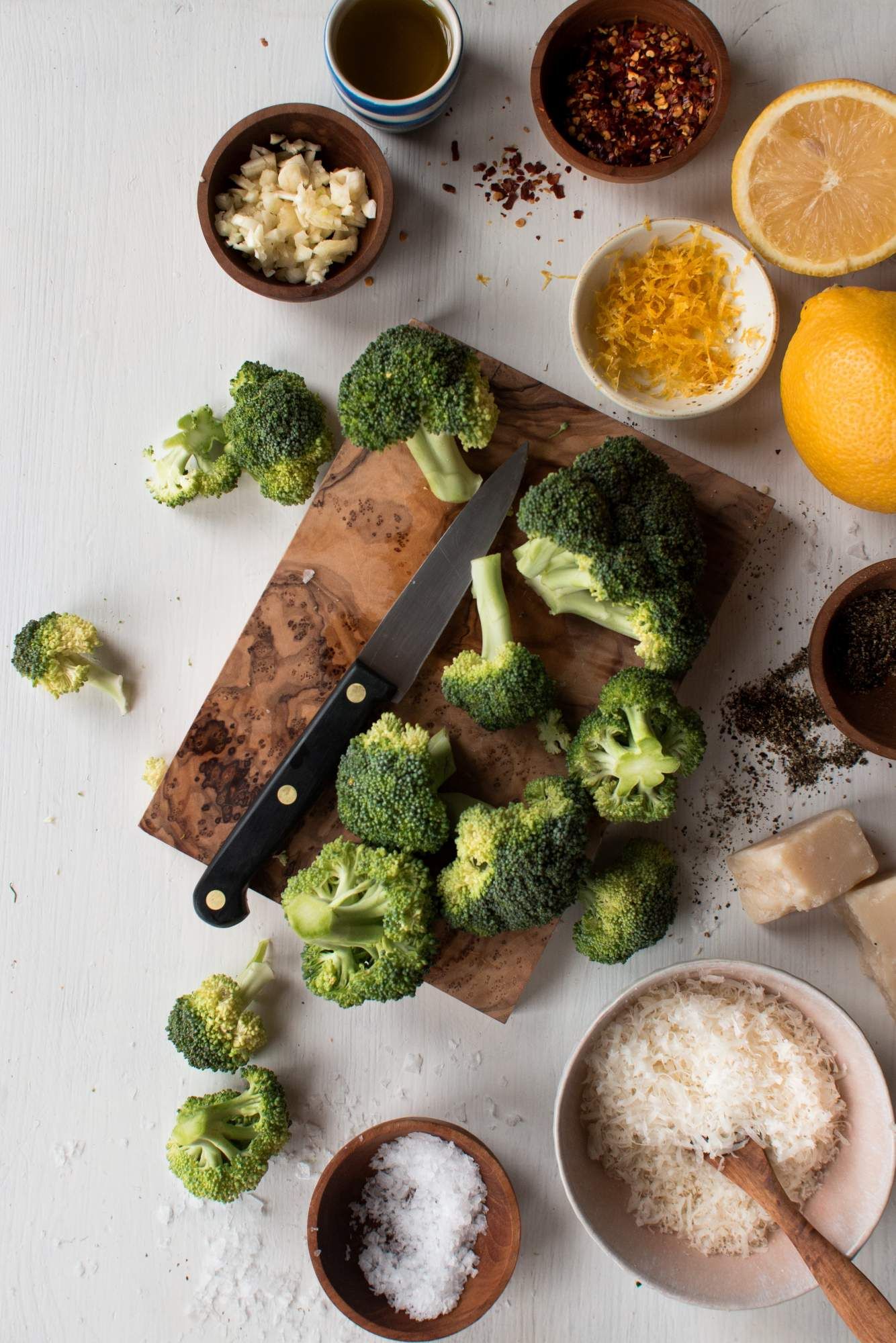 Ingredients for making sauteed broccoli including broccoli florets, olive oil, garlic, red pepper flakes, Parmesan cheese, and lemon.