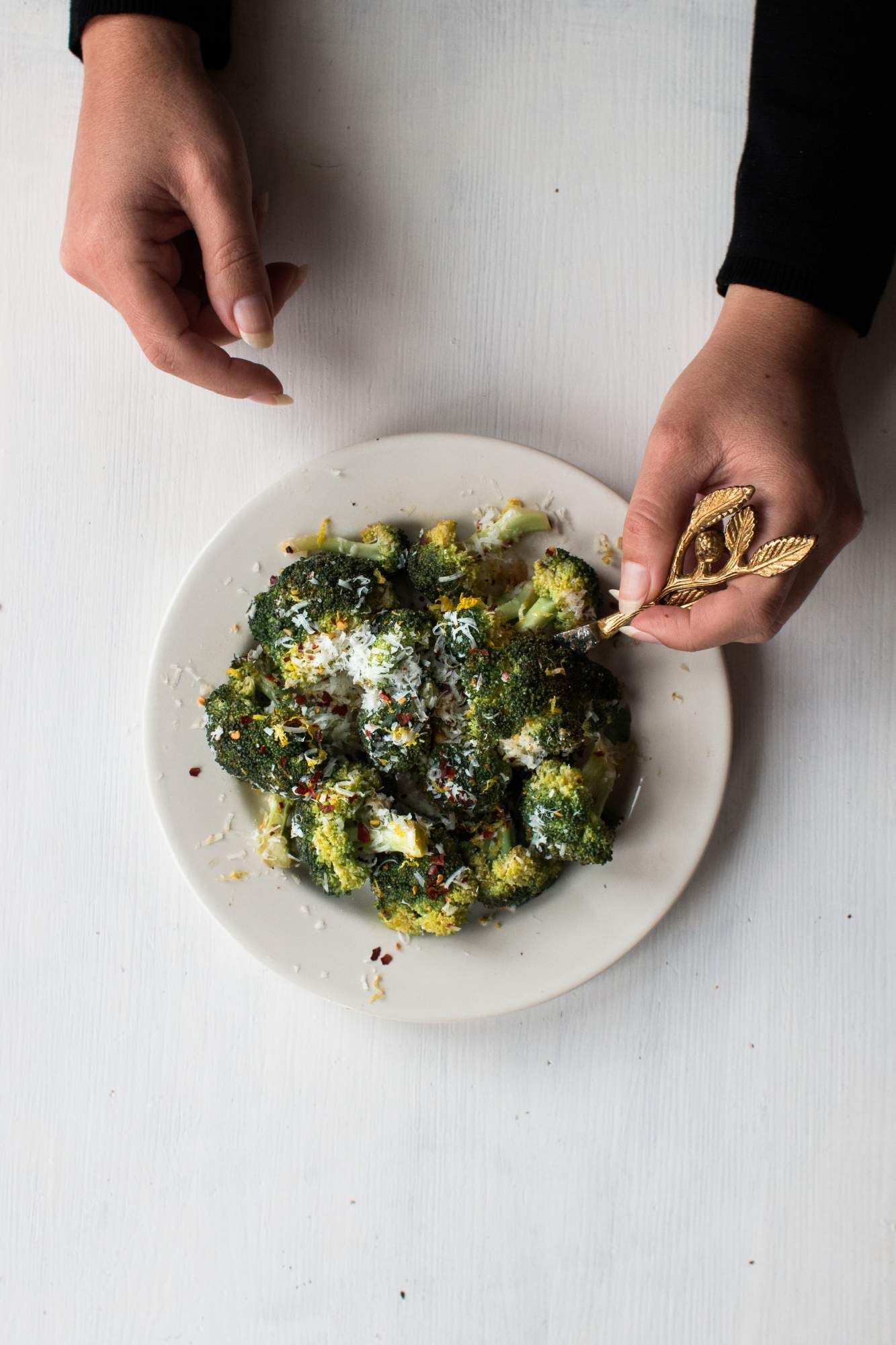 Garlic sauteed broccoli with Parmesan cheese and lemon in a bowl being held by two hands.