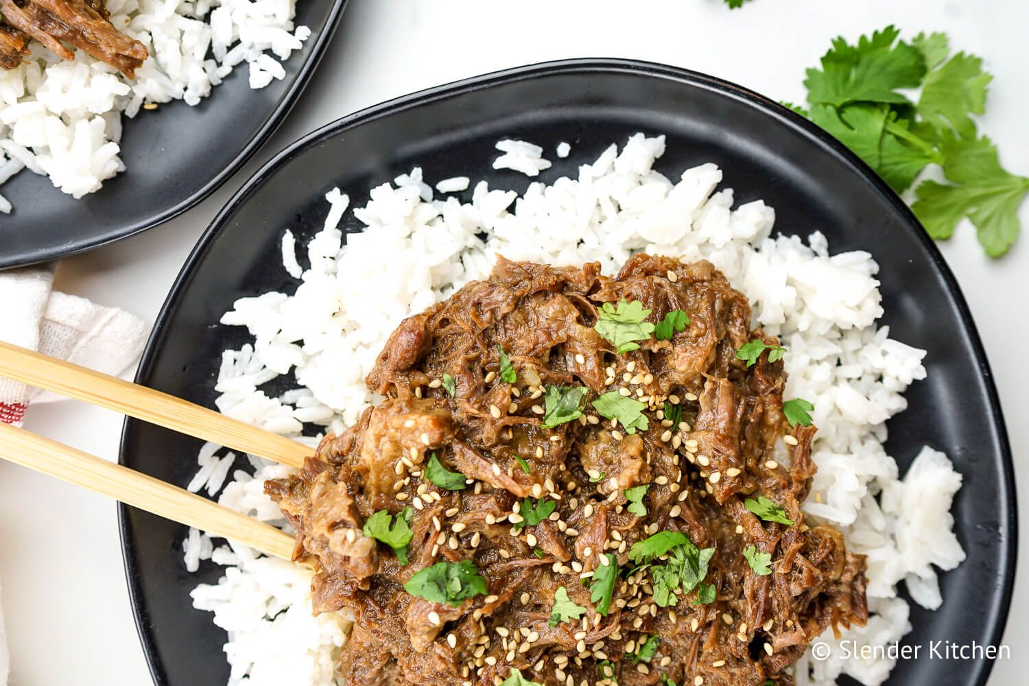 Slow Cooker Sesame Beef  over rice with sesame seeds and chopsticks.