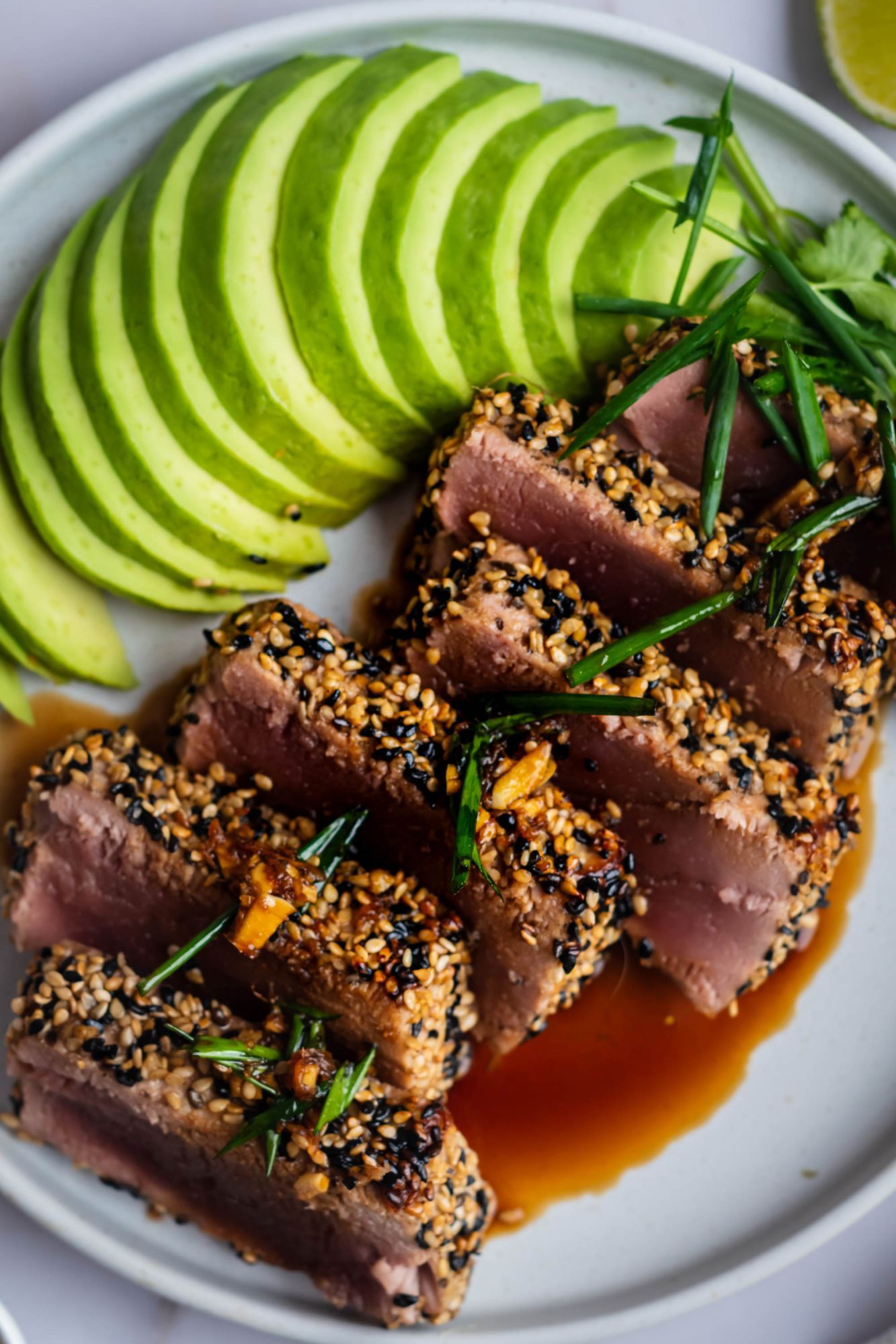 Seared tuna with a sesame crust sliced on a plate with avocado, soy sauce, and green onions.