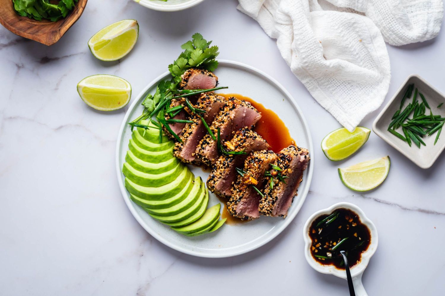 Sesame seared tuna with soy sauce and avocado on a white plate with limes on the side.