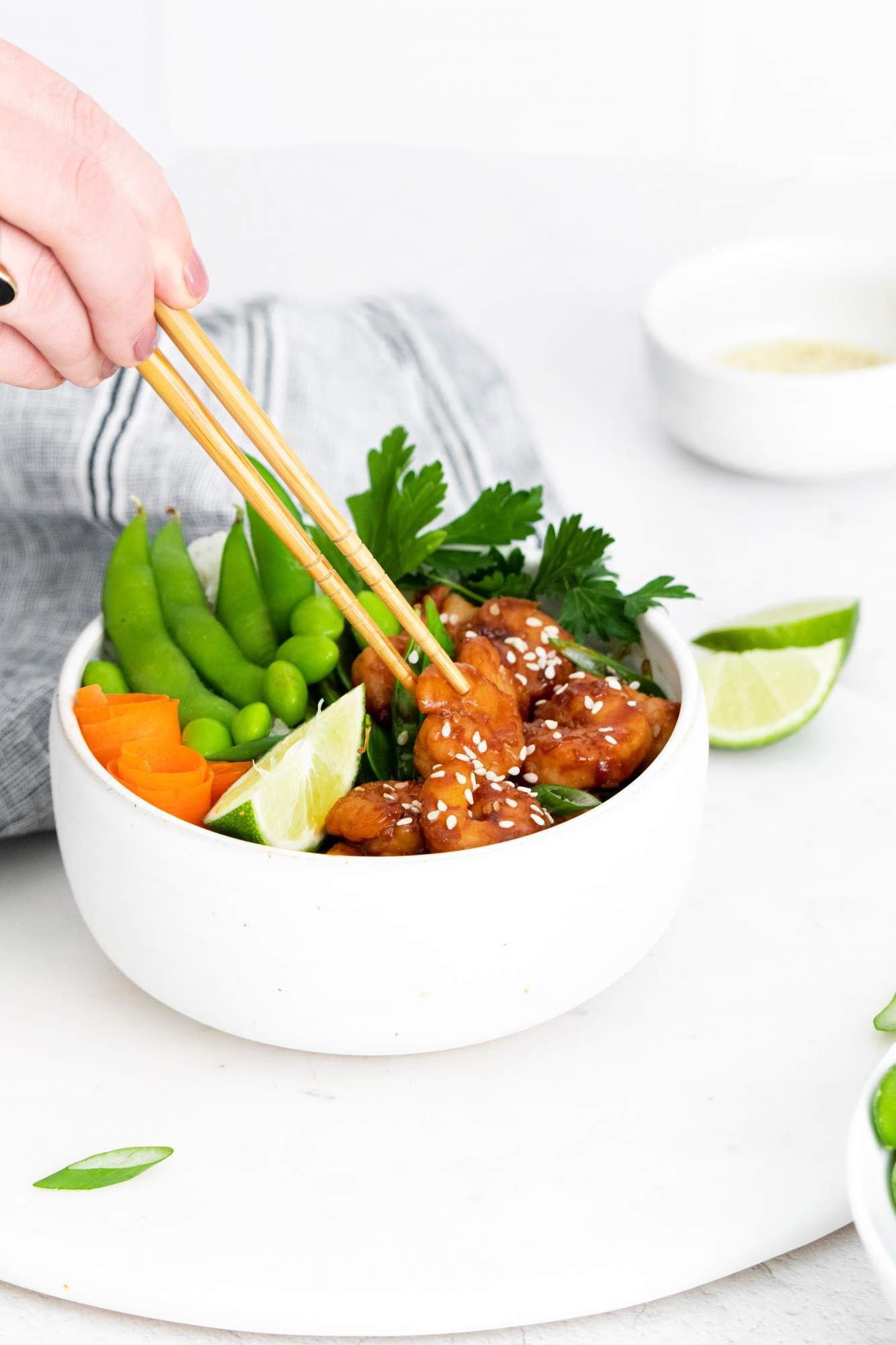 Asian sesame shrimp cooked in sesame sauce and served in a bowl with rice, vegetables, and chopsticks.