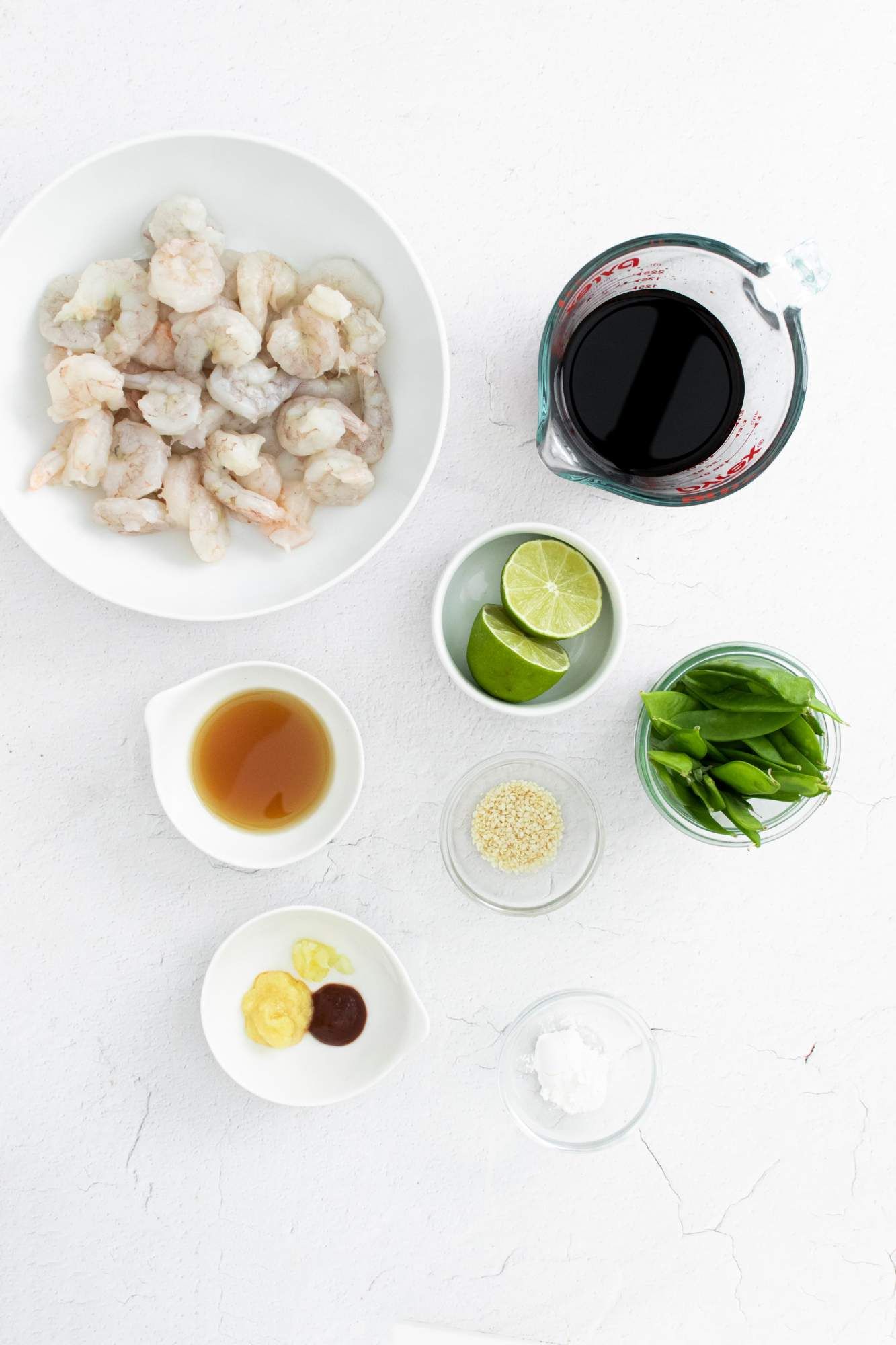 Ingredients to make sesame shrimp including raw shrimp, snow peas, soy sauce, sesame oil, lime juice, garlic, and ginger.