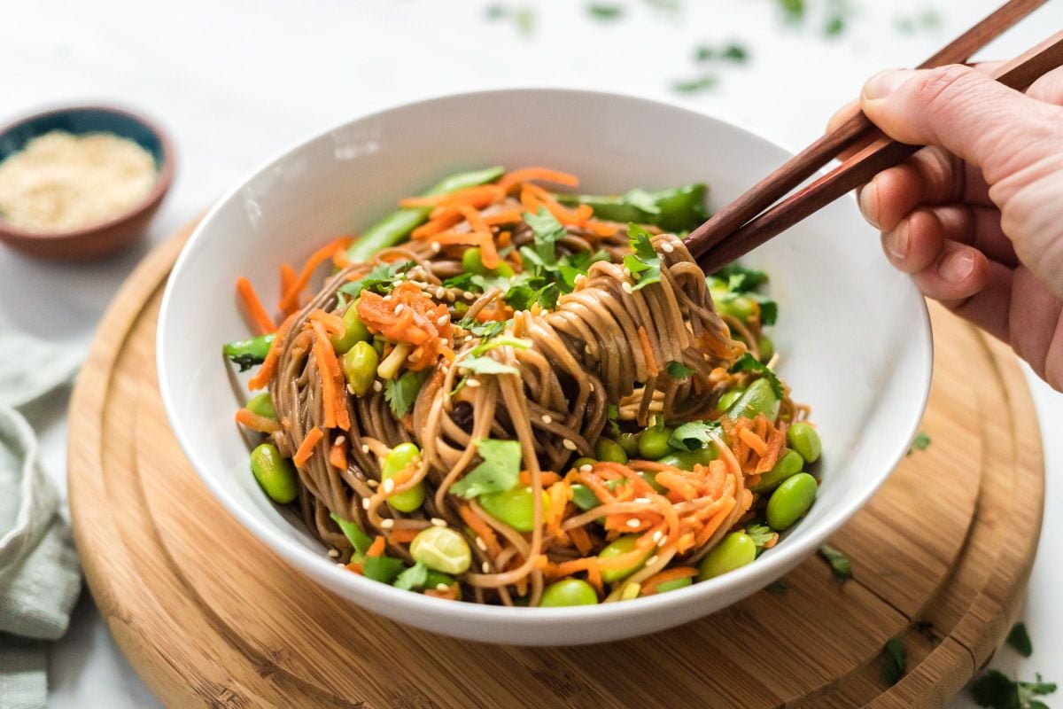 Asian soba noodle bowl with sugar snap peas, edamame, and carrots in a bowl with sesame seeds and sesame dressing.