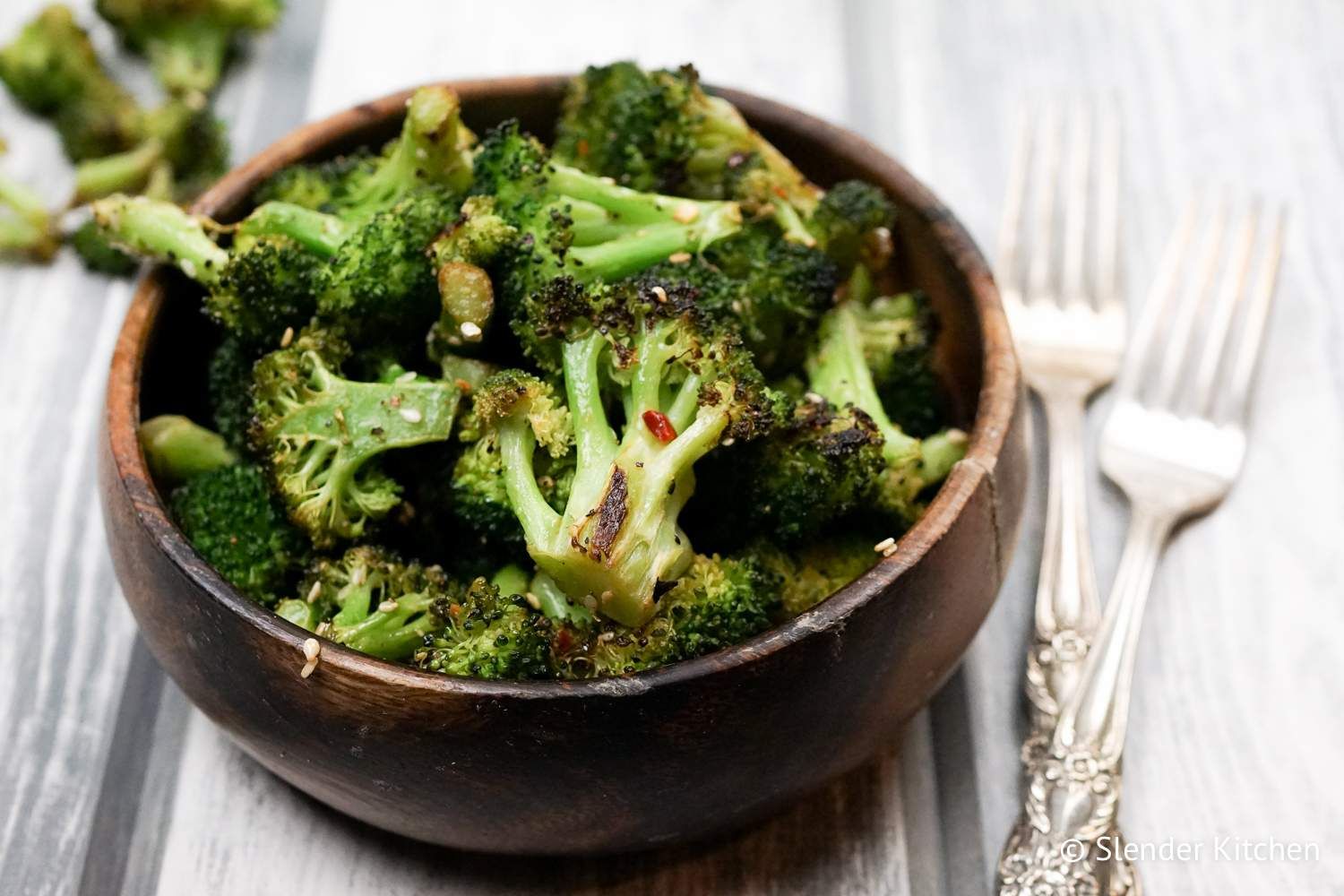 Roasted broccoli with sesame oil, soy sauce, garlic, and red pepper flakes in a wooden bowl.