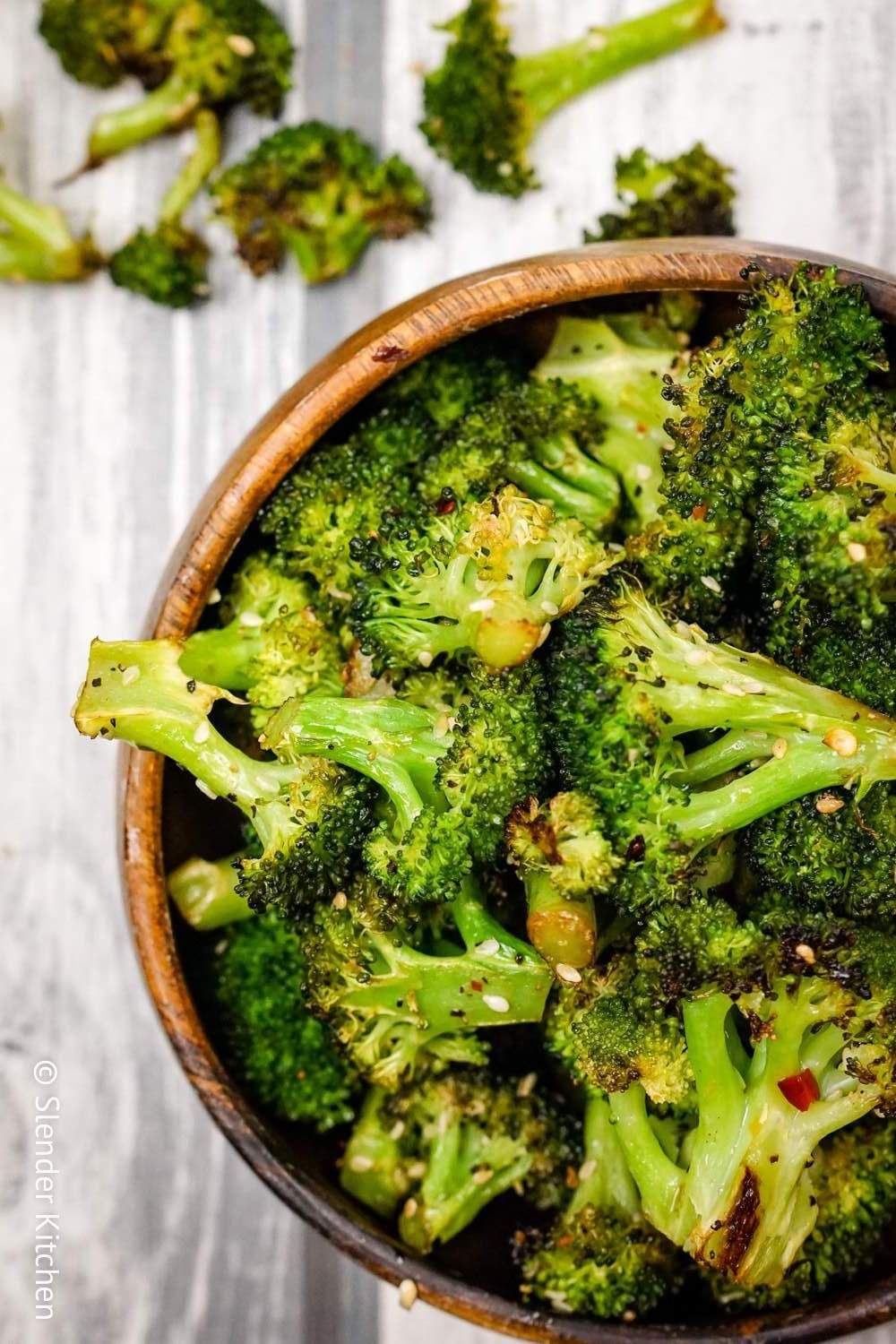 Sesame soy broccoli with minced garlic, soy sauce, sesame oil, and sesame seeds in a wooden bowl with florets on the side.