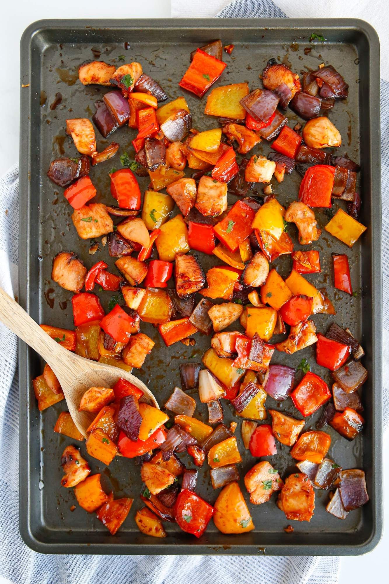 Sriracha and honey chicken on a sheet pan with bell peppers and red onions.