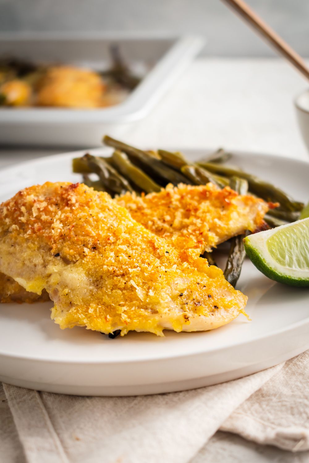 Sheet pan chicken breast with lemon pepper seasoning and breading served with roasted green beans on a plate.