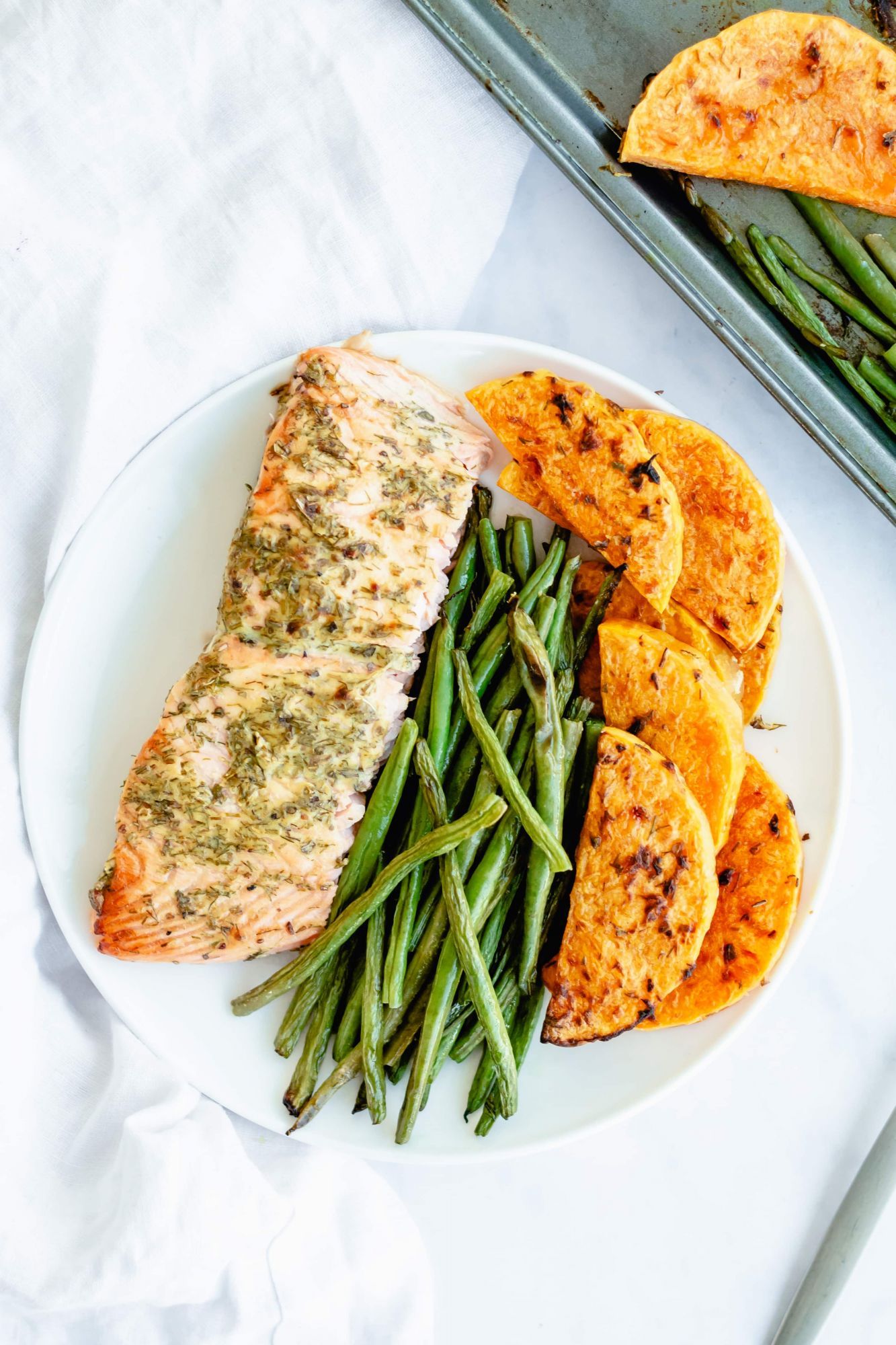 Baked salmon with green beans and butternut squash cooked on a single sheet pan and served on a white plate.